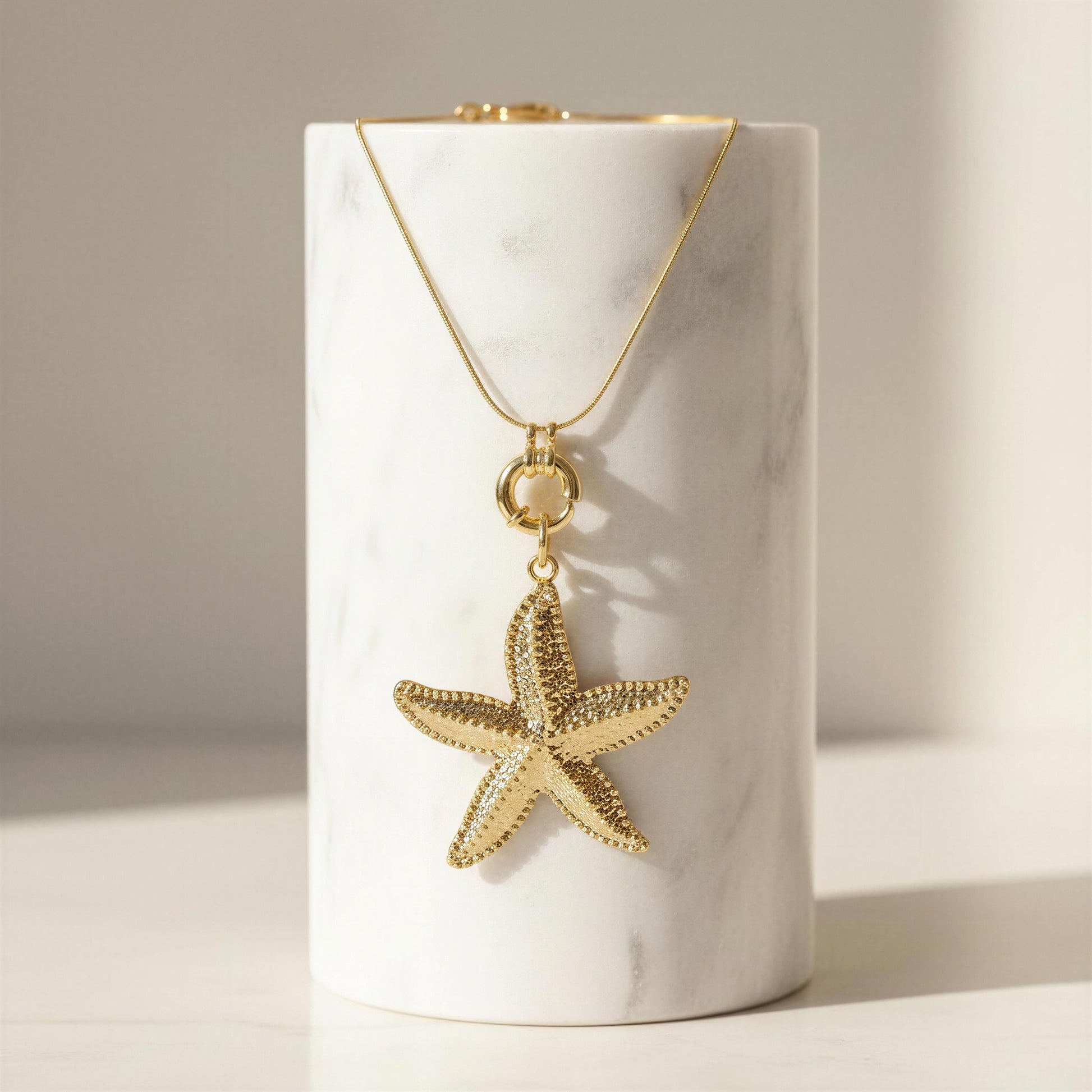 Gold starfish pendant necklace on a white cylindrical stand with a neutral background