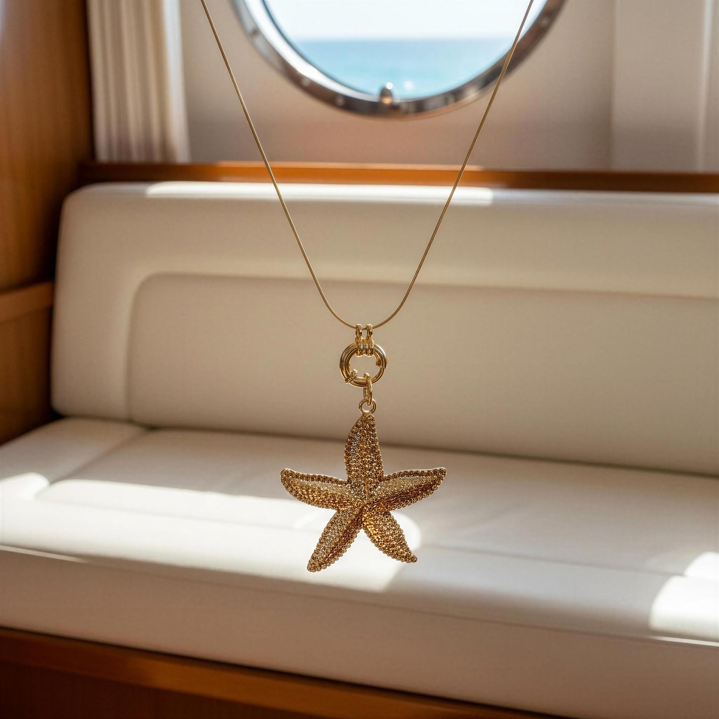 Gold starfish pendant necklace from Chica Chica Jewelry on a white cushion with a window in the background