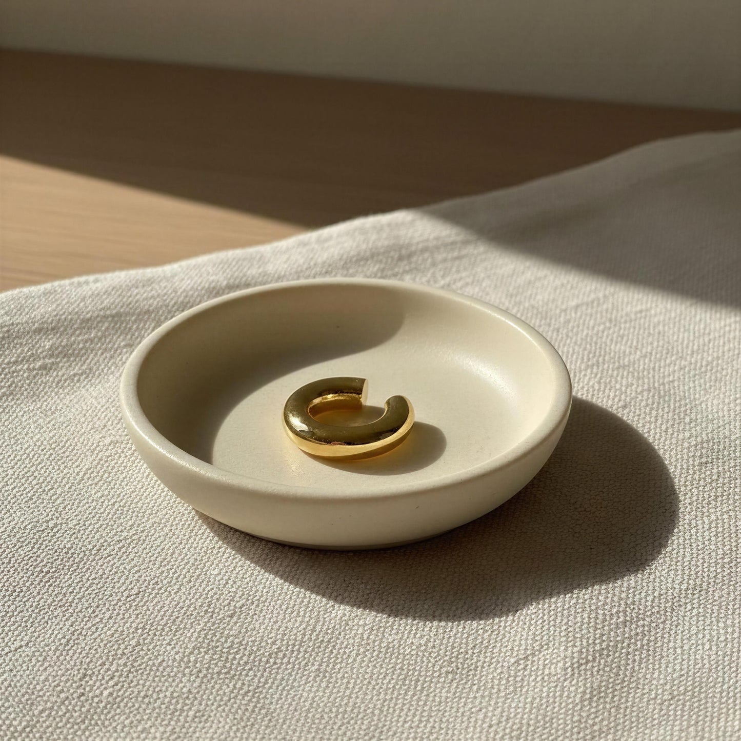 Beige ceramic dish with the Stellar Arc Ear Cuff on a beige fabric background
