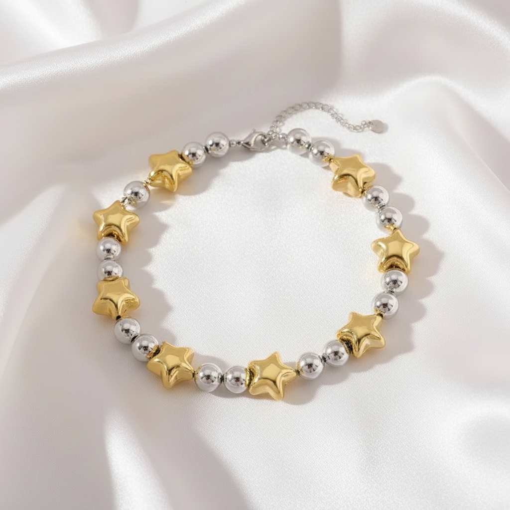 Gold and silver star bead bracelet resting on soft white silk fabric, highlighting the bracelet’s smooth finish and star details.
