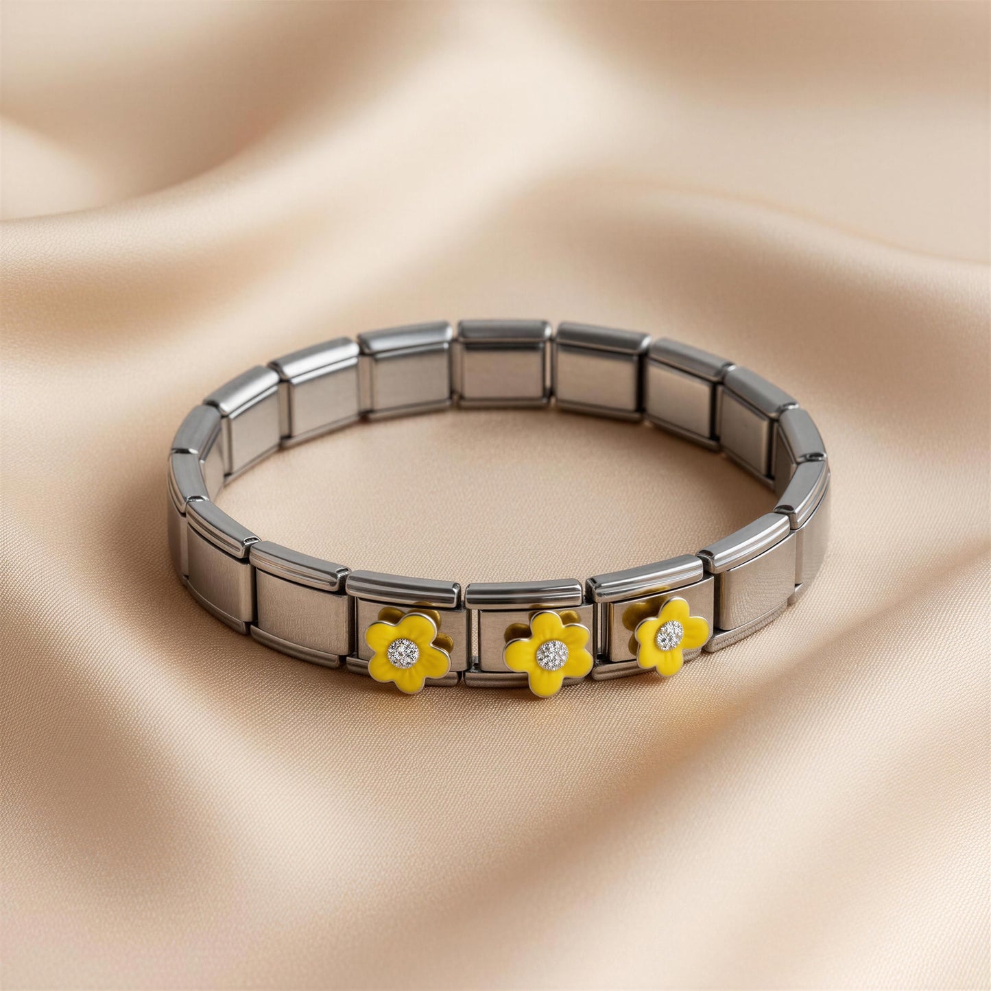 Silver Italian bracelet from Chica Chica Jewelry with yellow flower-shaped charms on a beige fabric background