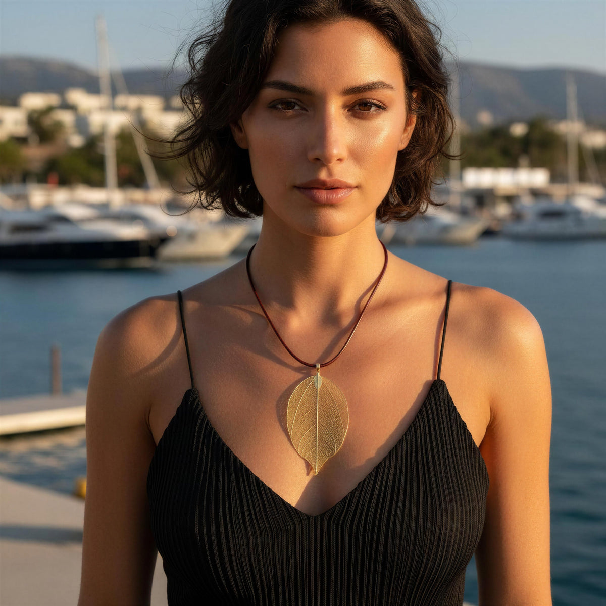 Model wearing a silk pleated straps black dress by a Mediterranean marina and the Aurelia Necklace from Chica Chica Jewelry.