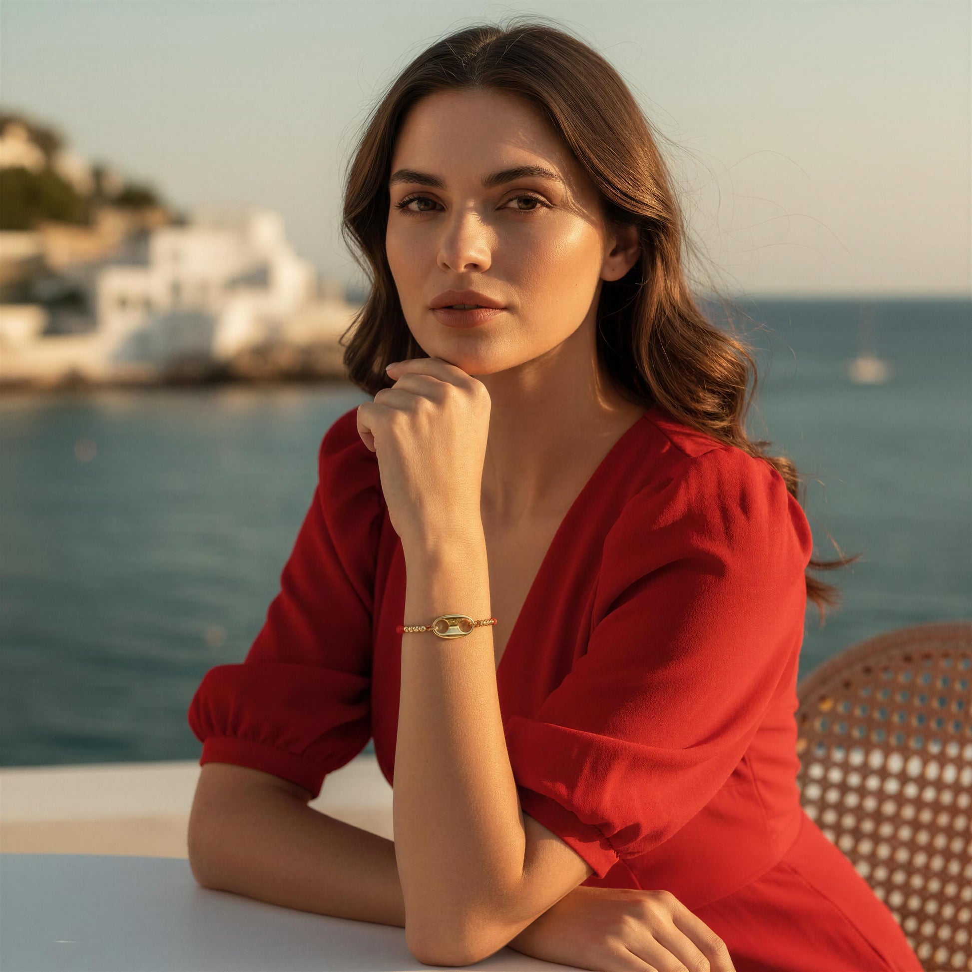 Woman in a red dress sitting by the sea with a scenic background wearing the Nexo Bracelet – Red