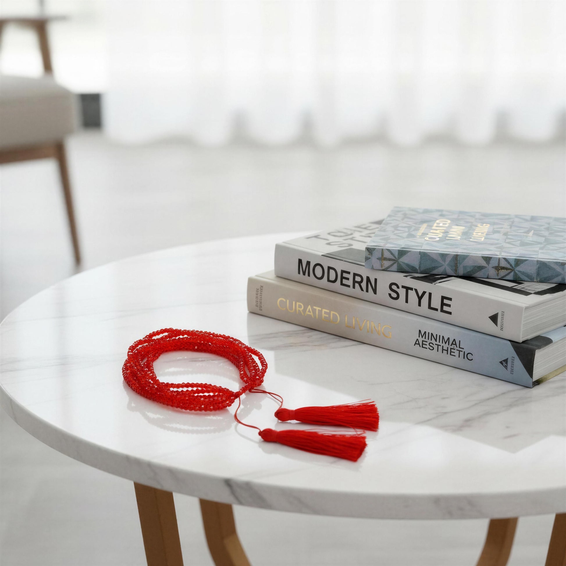 Red beaded bracelet with tassels on a marble table with books in the background
