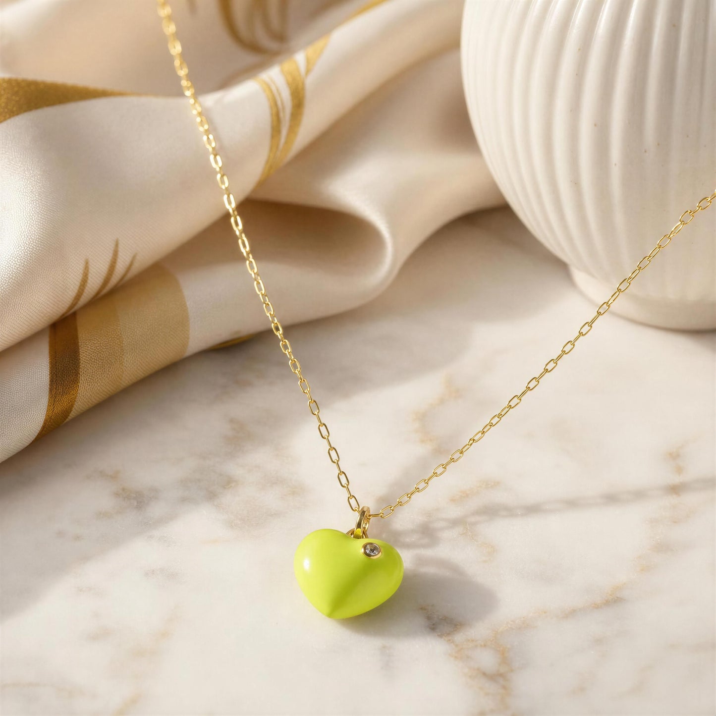 Necklace with a heart-shaped lime green pendant on a marble surface with fabric in the background