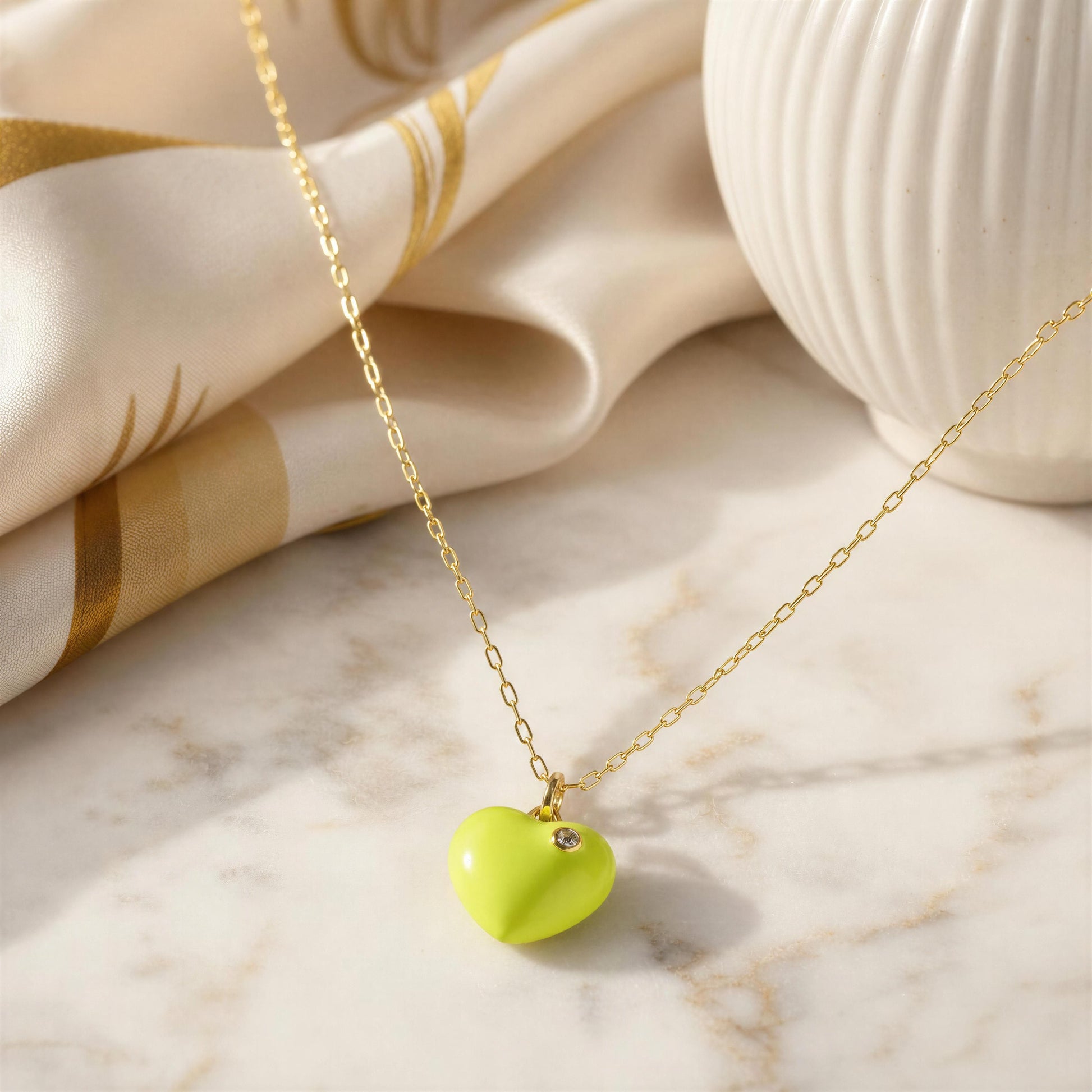 Necklace with a heart-shaped lime green pendant on a marble surface with fabric in the background