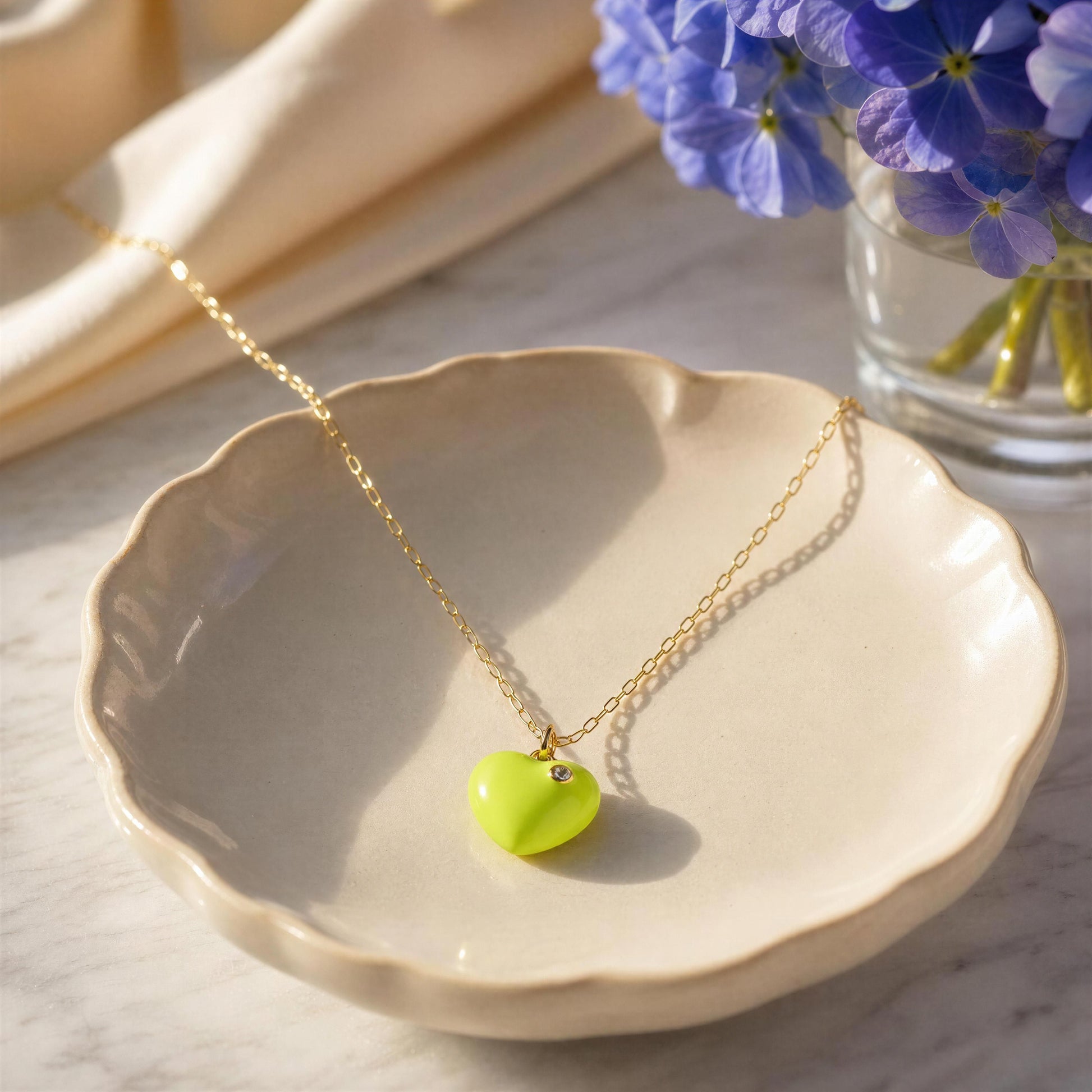 The Amore Lemon Glow Heart Necklace on a beige dish with flowers in the background