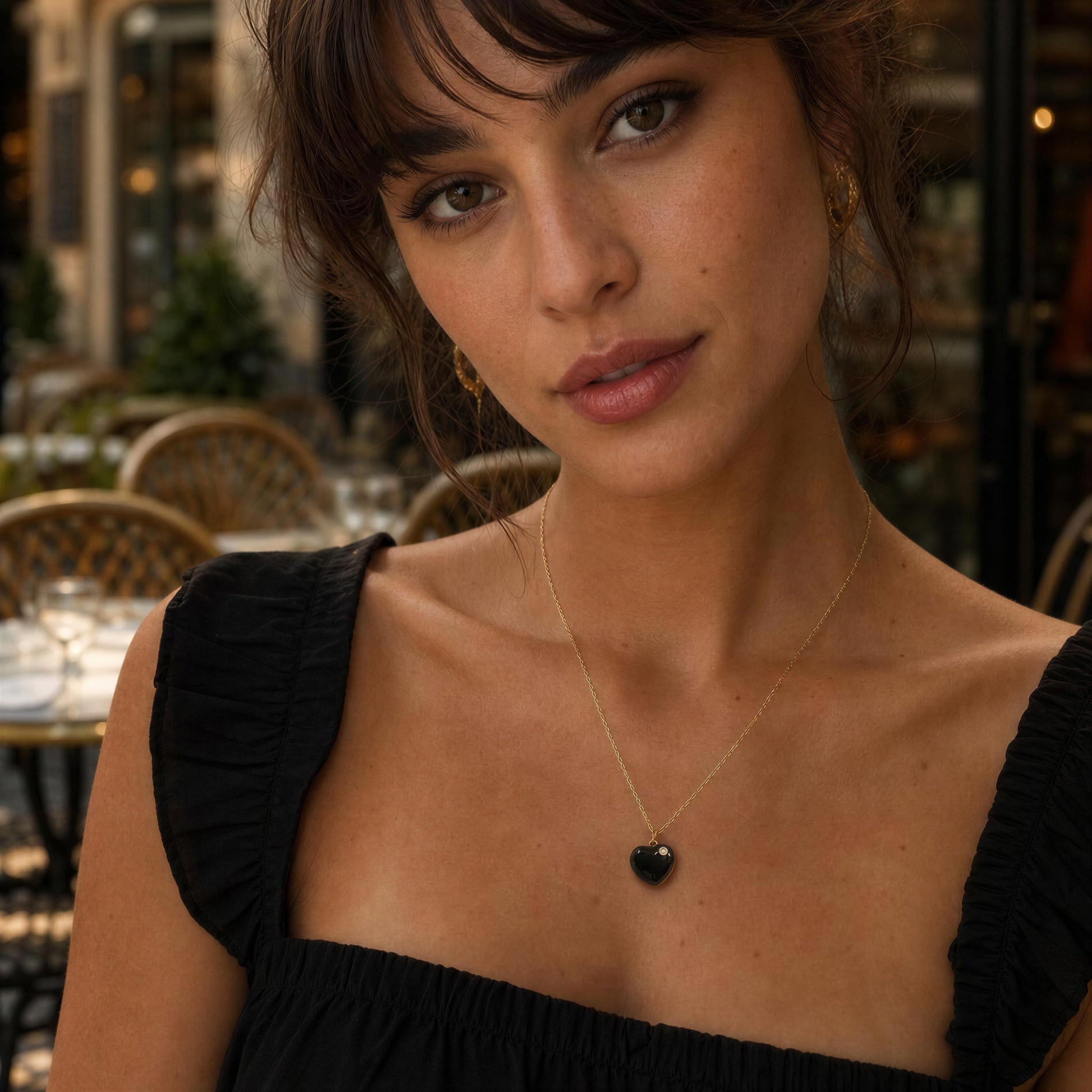 Woman wearing a black top and the Amore_Noir_Heart_Necklace sitting at outdoor setting