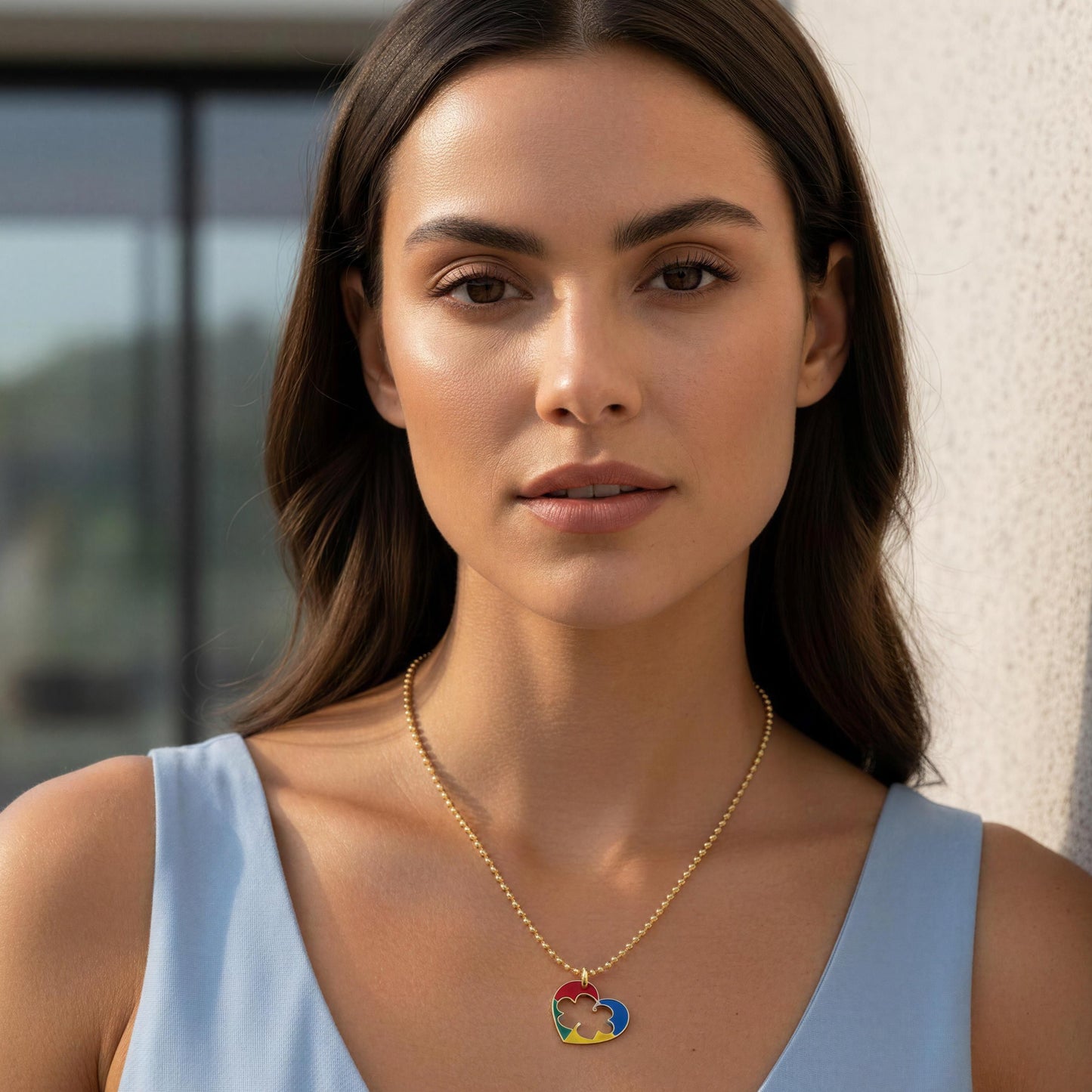 Woman wearing a gold necklace with a colorful pendant against a neutral background