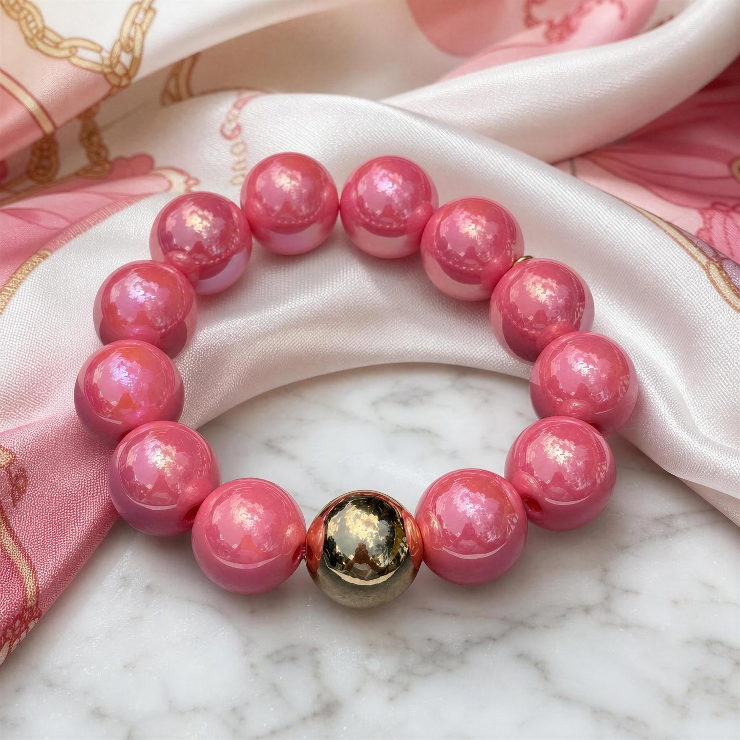Pink beaded bracelet with a gold accent on a marble surface with pink fabric background
