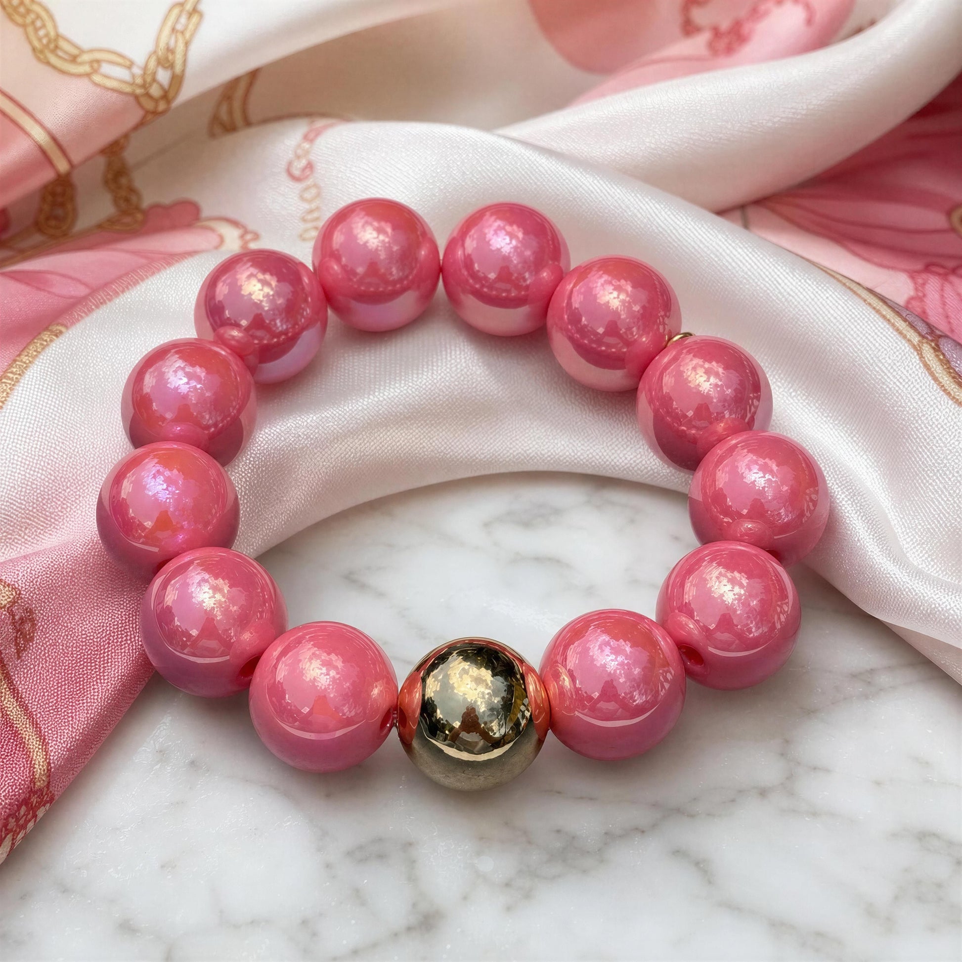Pink beaded bracelet with a gold accent on a marble surface with pink fabric background