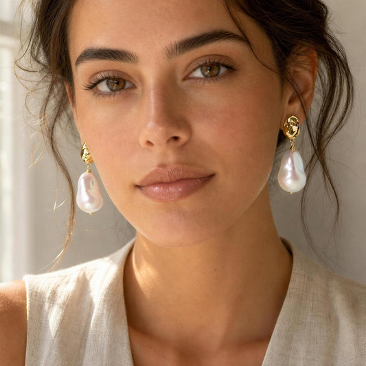 A close-up of a woman wearing the Bellina_Pearl_Drop_Earrings from _Chica_Chica_Jewelry paired with a light beige linen top.