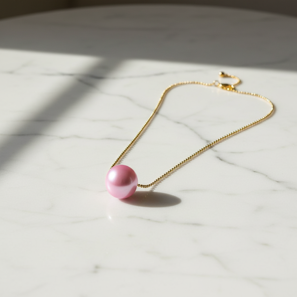 Blush Petite Sphere Necklace with a pink bead on a marble surface