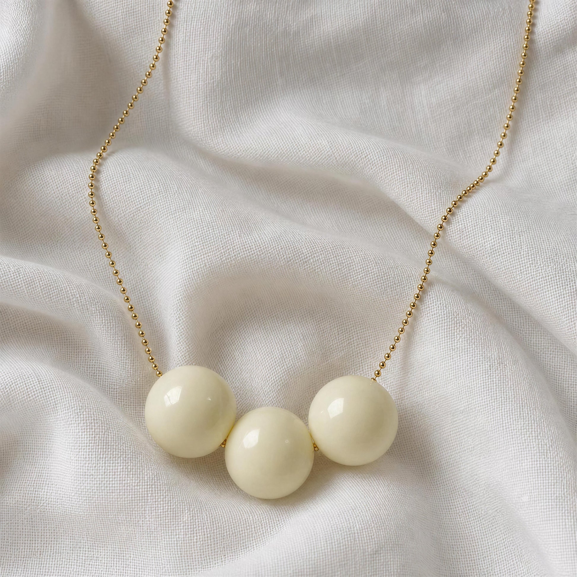 Necklace with three white beads on a gold chain against a white fabric background