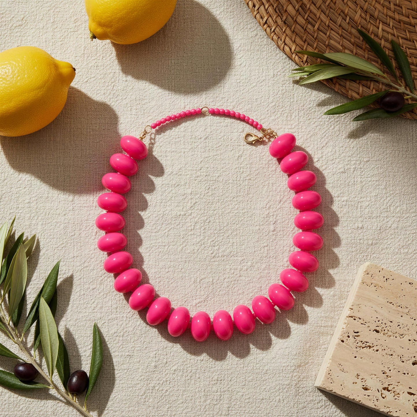 The Capri Fuchsia Statement Choker on a textured surface with lemons and leaves