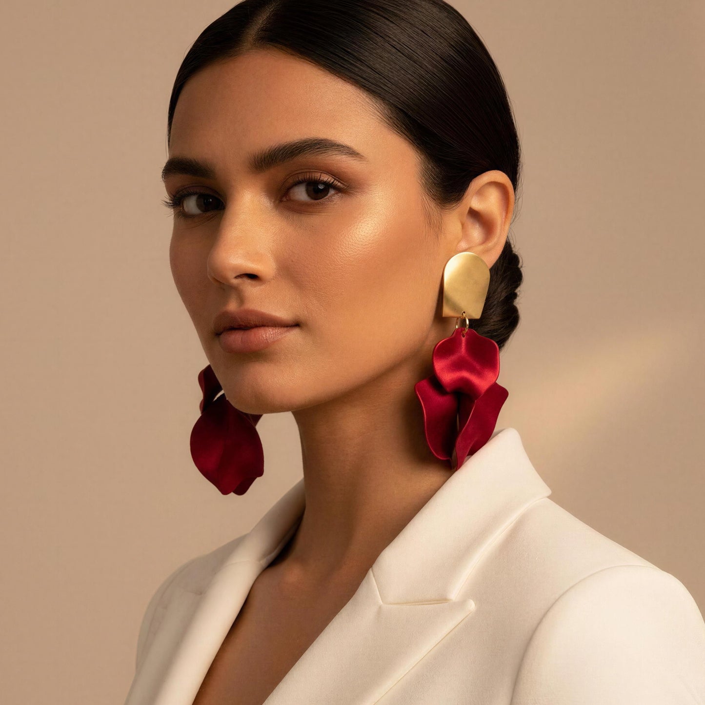 Woman wearing a white blazer and red floral earrings against a beige background