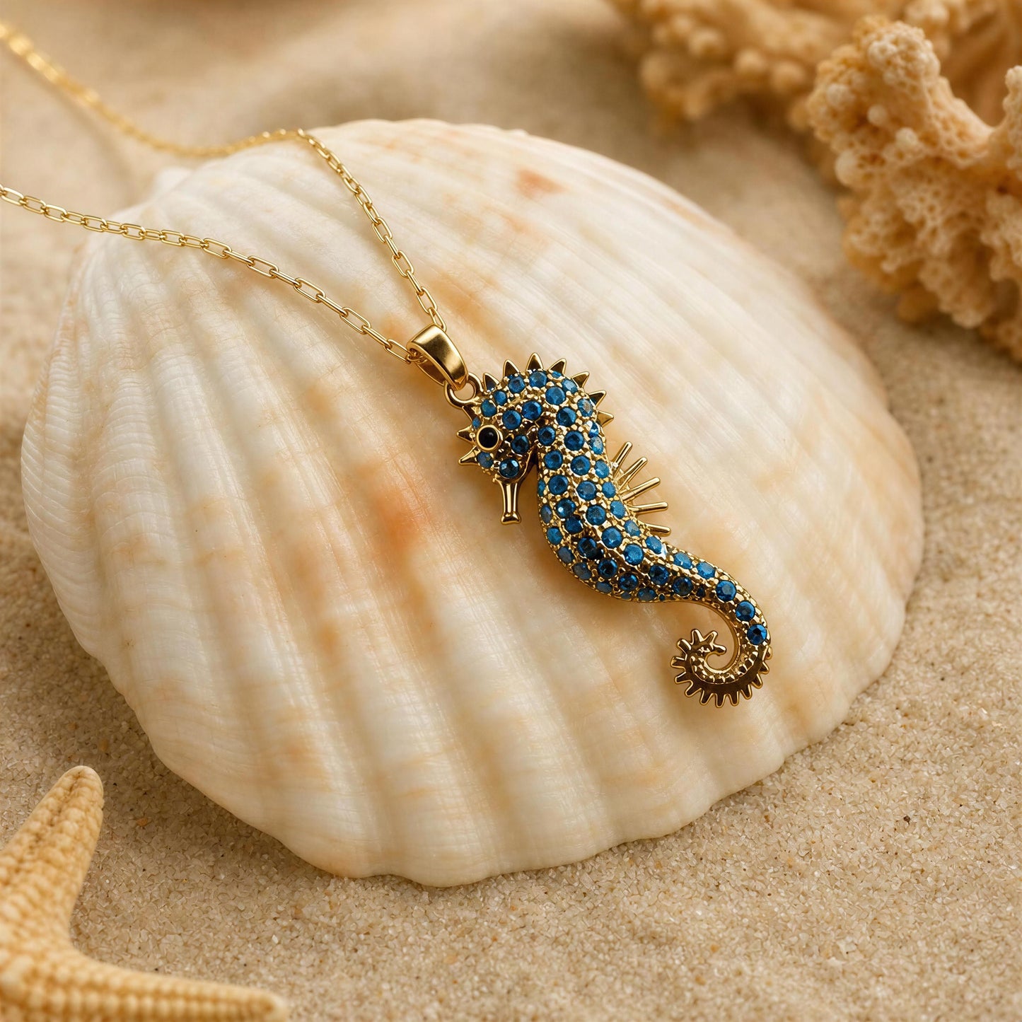 The Denizati Necklace, an 18K gold-plated seahorse pendant necklace,, displayed on a large beige seashell over sand with coral and a starfish.