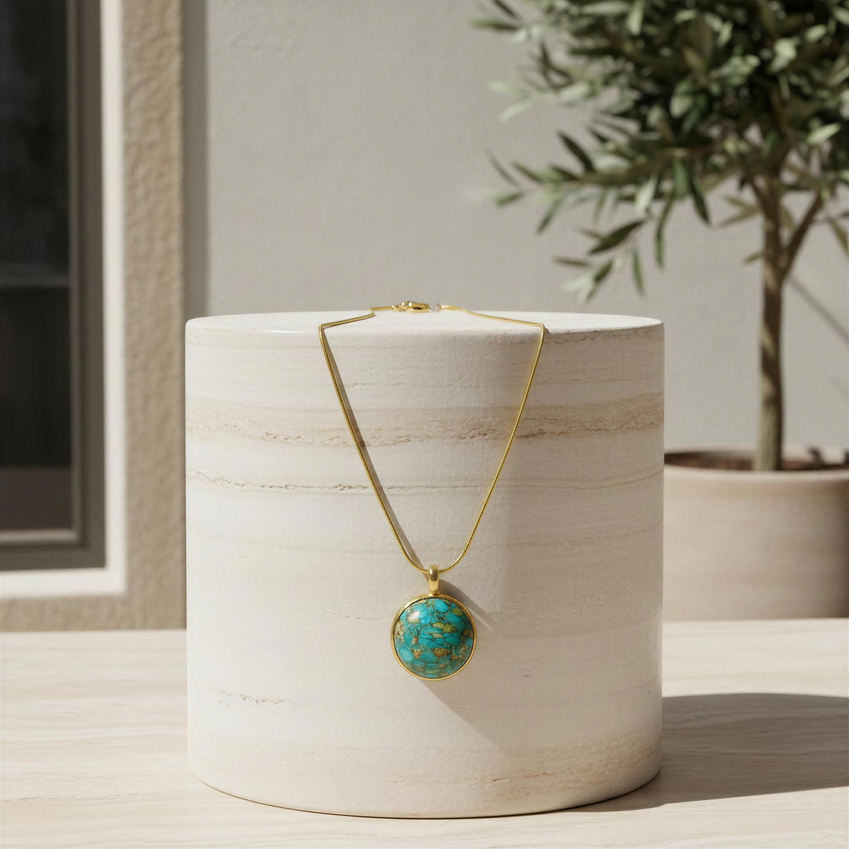 The Derya Necklace from Chica Chica Jewelry against a marble tall pedestal, indoor setting. 