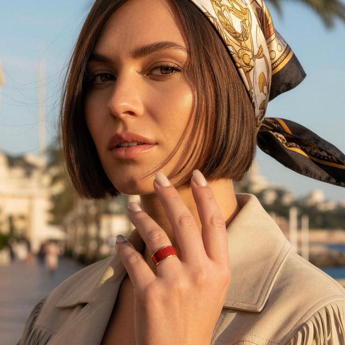 Model wearing a suede crème color jacket and  the Duna Ring – Carmine from Chica Chica Jewelry on outdoor promenade. 