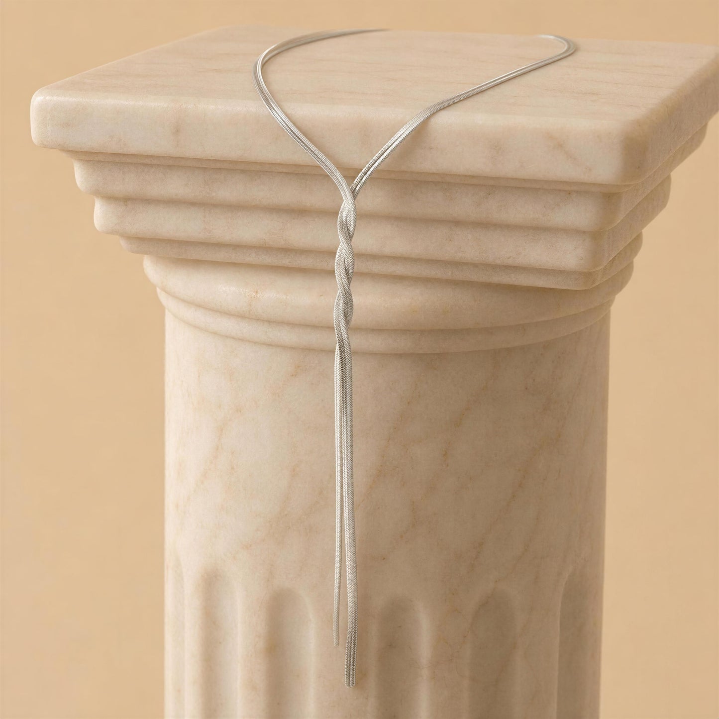 The Eterna Lariat Necklace - Silver on a marble column against a beige background