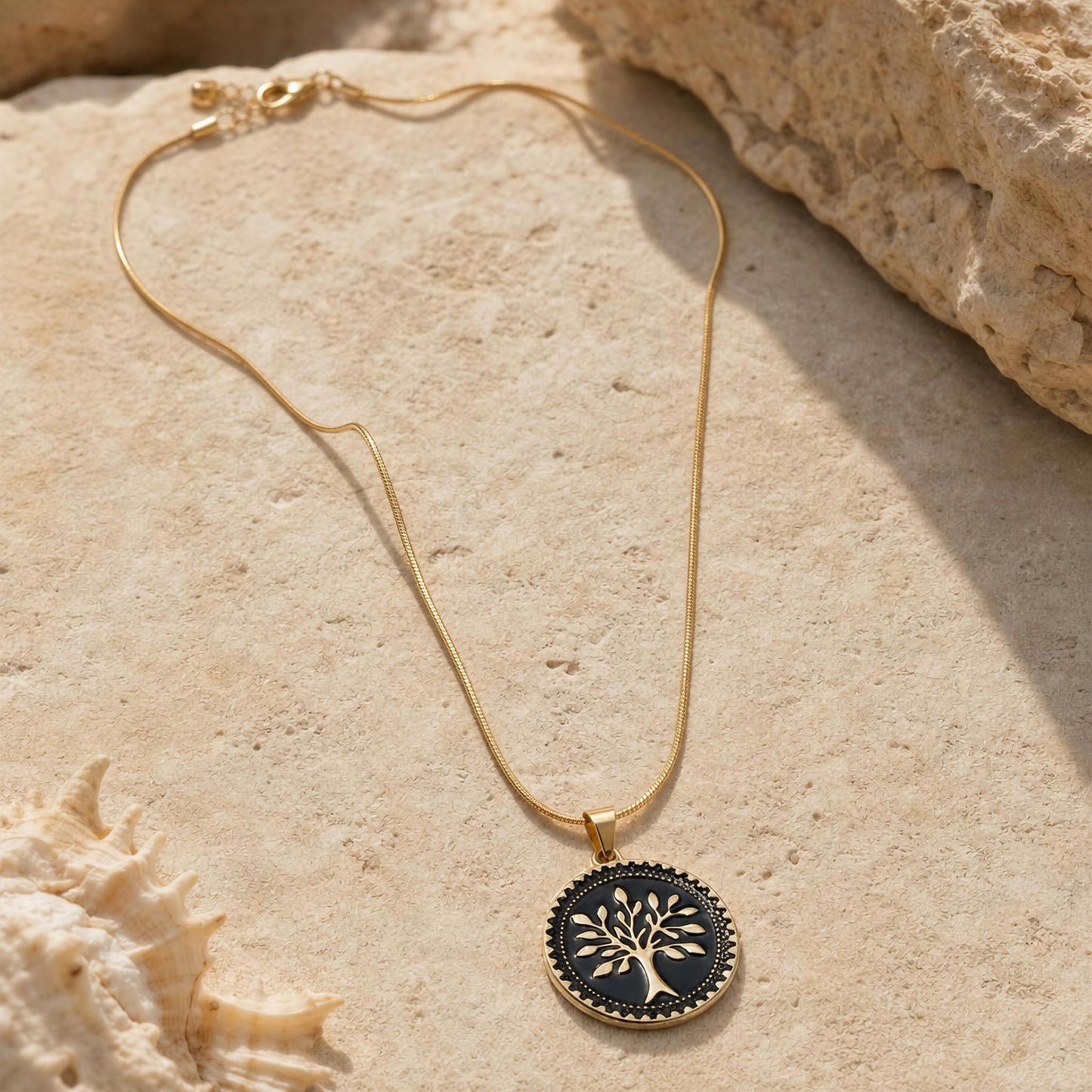 Gold necklace with a black pendant featuring a tree design on a beige stone surface.