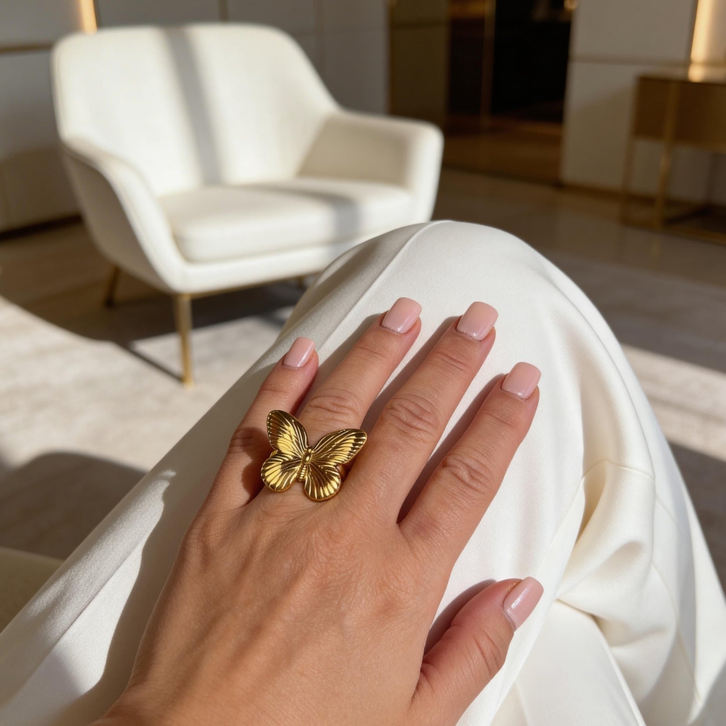 Hand wearing the  Forever Flutter Ring - Gold  with a blurred indoor background