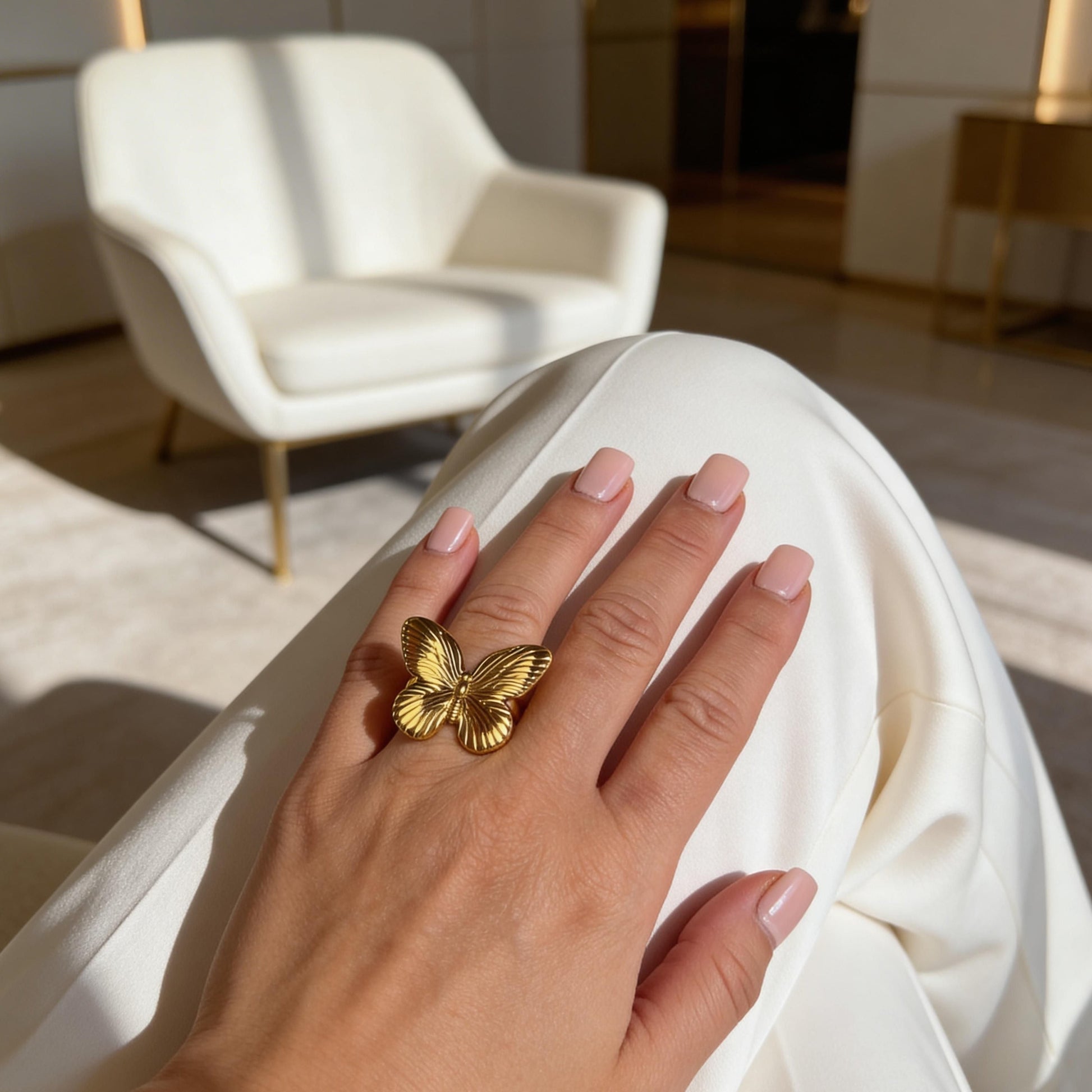 Hand wearing the  Forever Flutter Ring - Gold  with a blurred indoor background