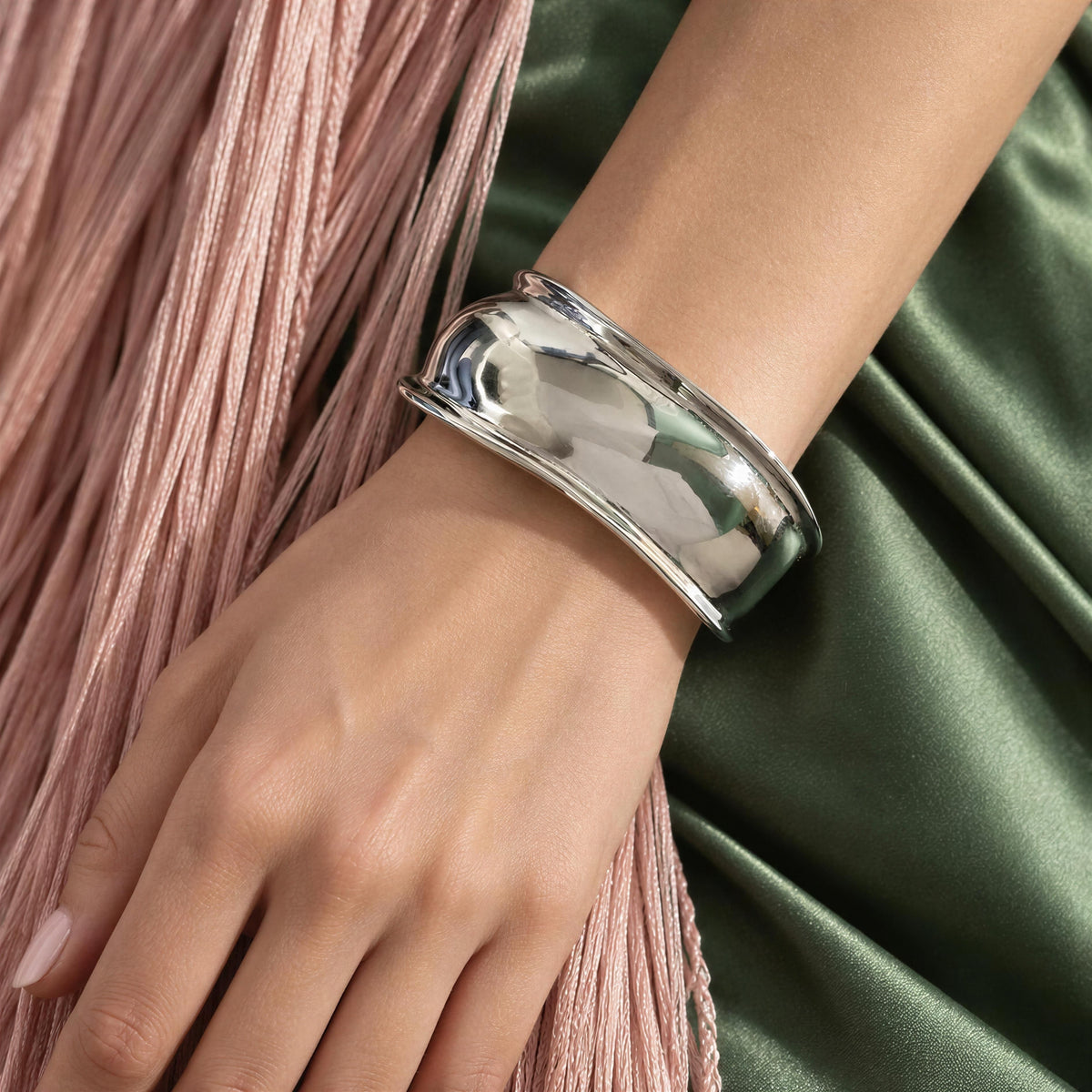 Model’s hand wearing the Forma Cuff Silver from Chica Chica Jewelry against silk green fabric and pink fringes.