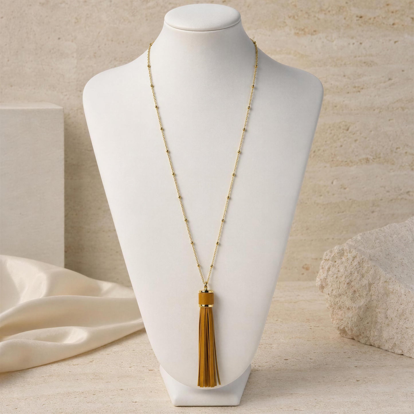 The Frangia Cammello Necklace from Chica Chica Jewelry, on a white jewelry bust against a warm beige textured background.