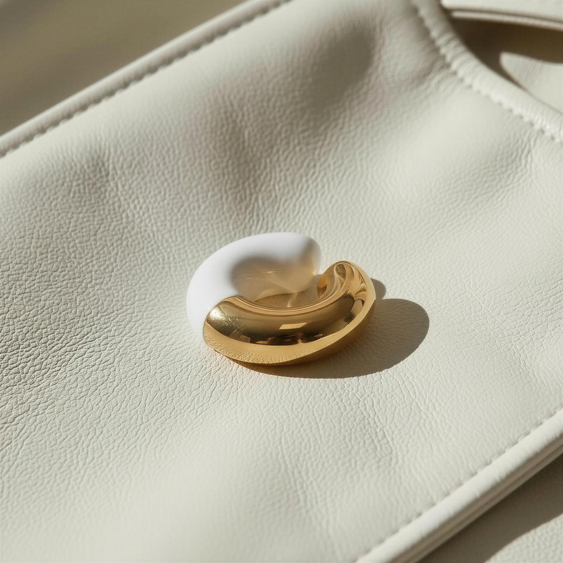 Close-up of a white and gold ear cuff on a beige leather surface