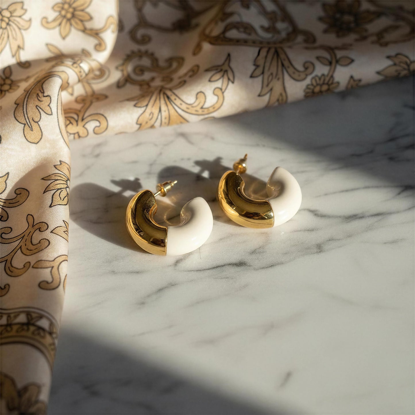 Gold and white earrings on a marble surface with patterned fabric in the background