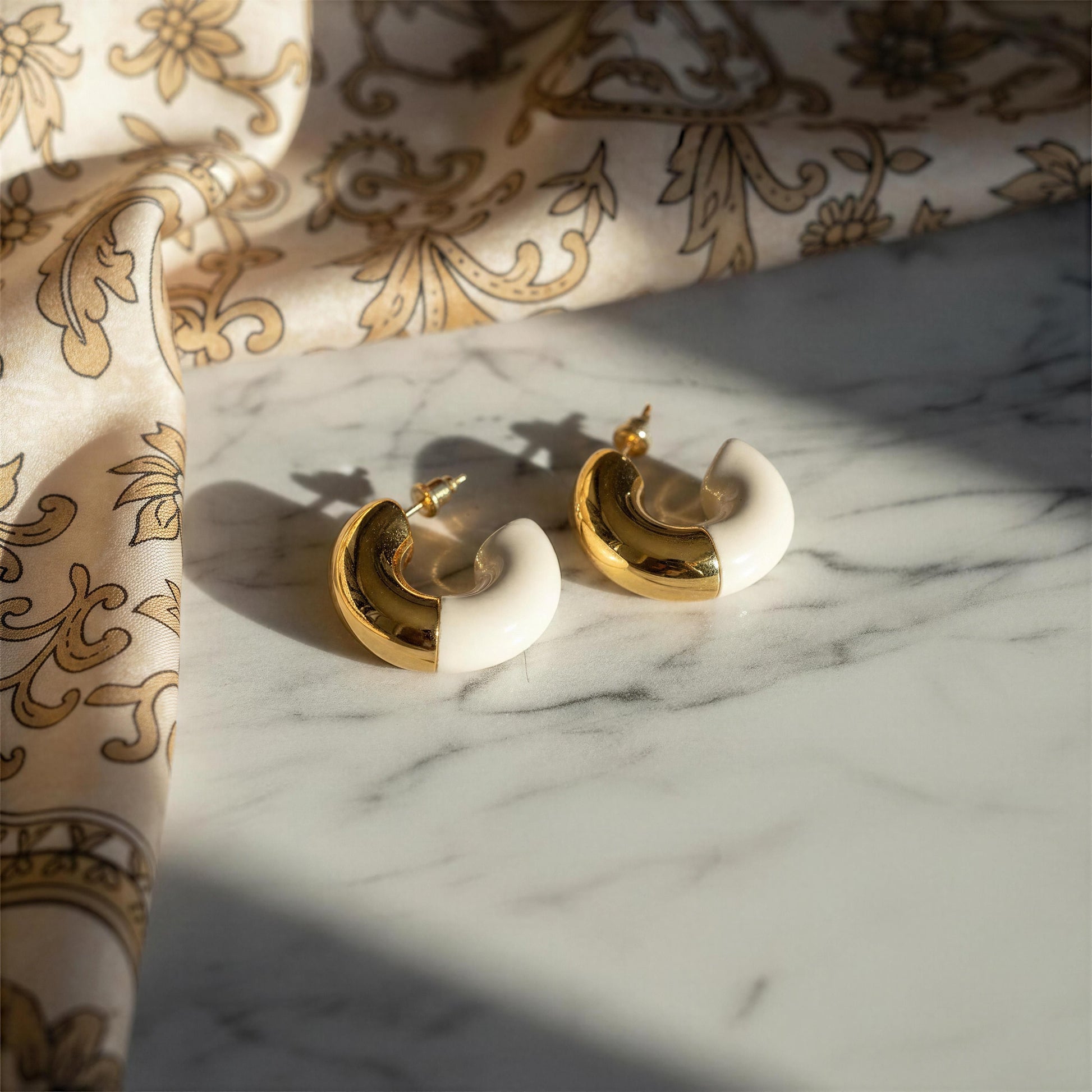 Gold and white earrings on a marble surface with patterned fabric in the background