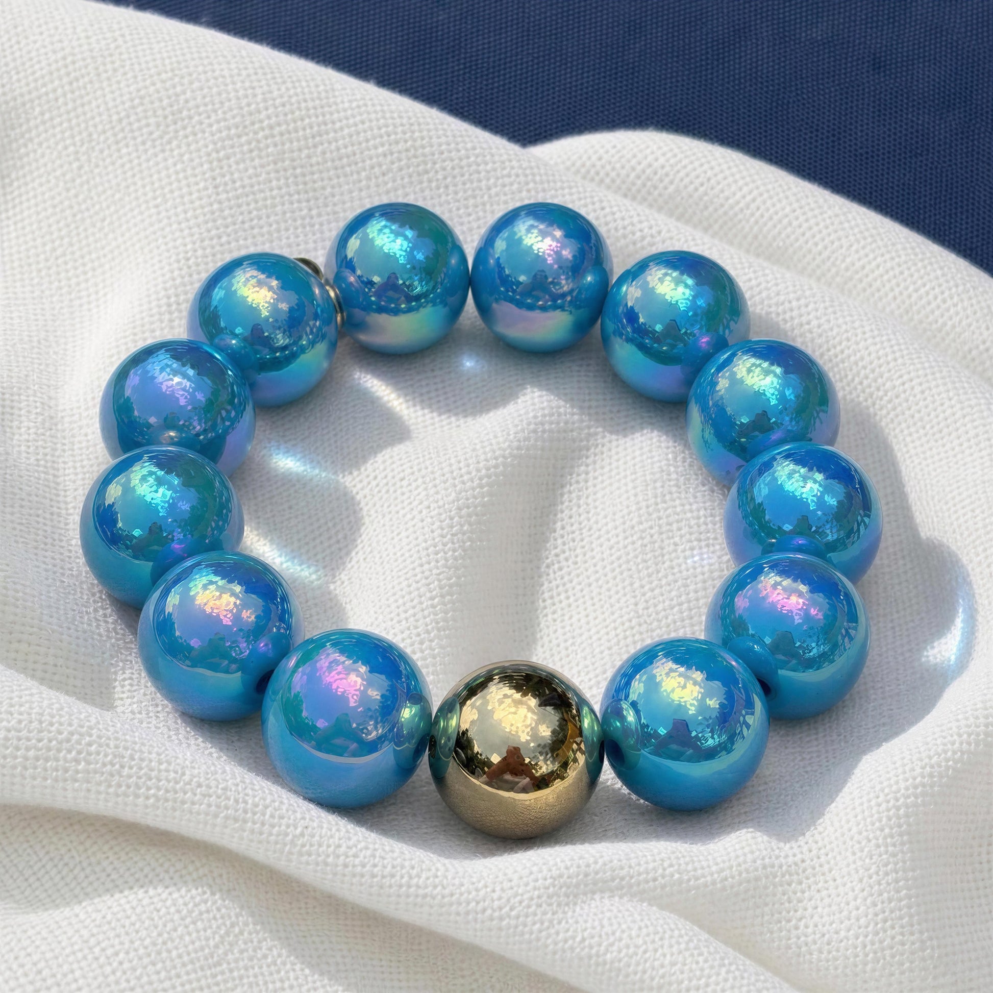 Blue beaded bracelet with a gold accent on a white fabric background