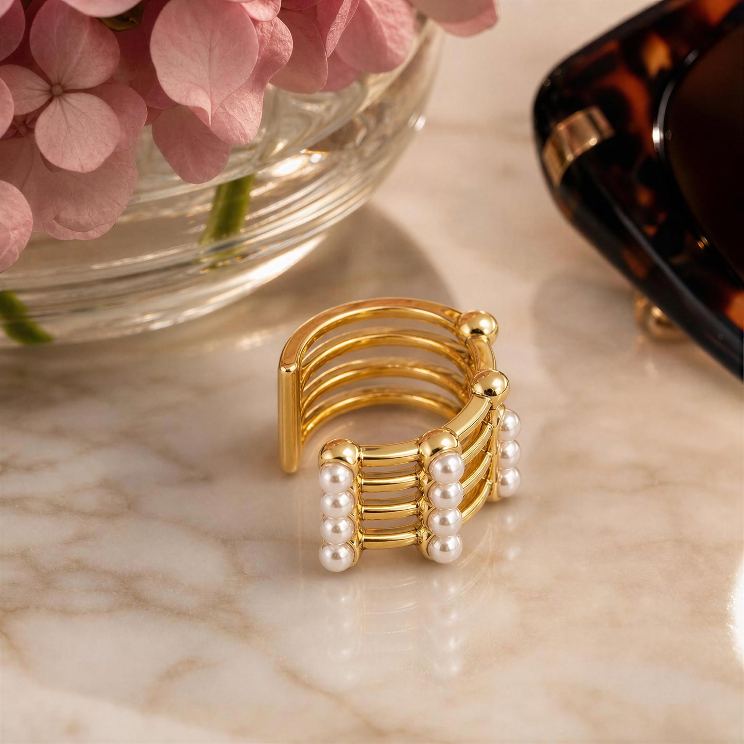 The Grid Pearl Ear Cuff on a marble surface with pink flowers and a tortoiseshell sunglasses in the background.