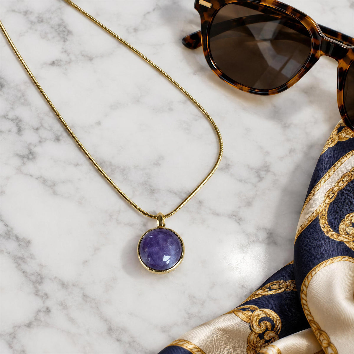 The Lavanda Necklace from Chica Chica Jewelry against white marble table next to sunglasses and silk scarf. 