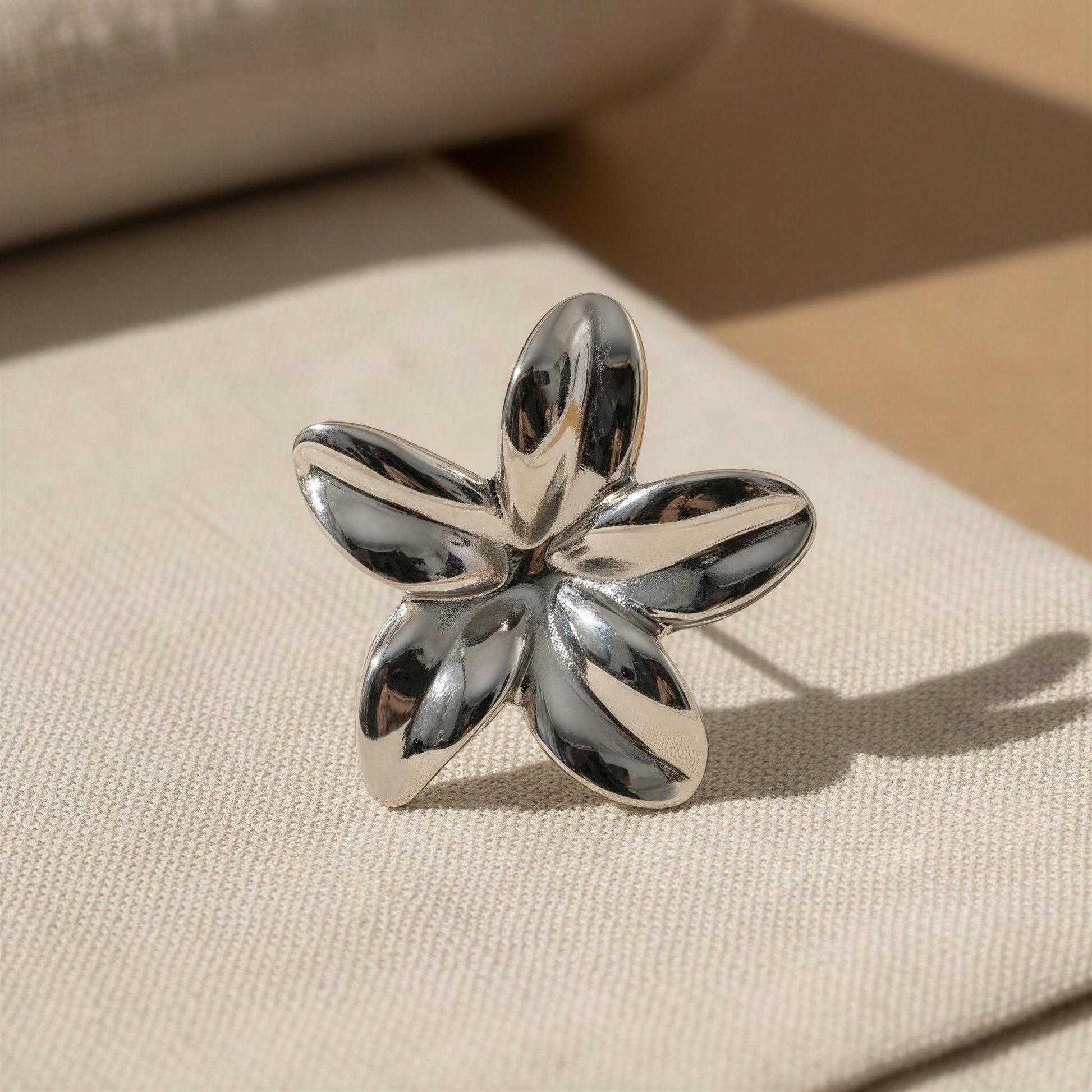 Silver flower-shaped ring on a beige fabric background