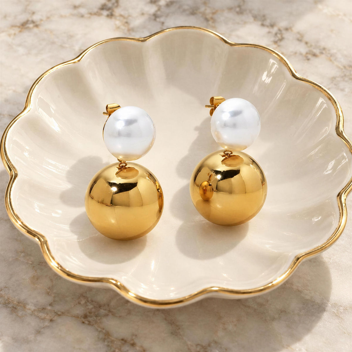 Lustra Gold & White Drop Earrings featuring luminous white pearl accents and shiny gold spheres displayed in an elegant dish.
