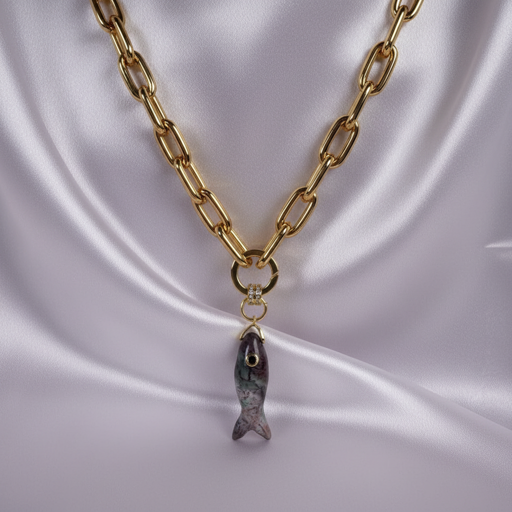 The Marea Fish Necklace from Chica Chica Jewelry with natural gemstone fish pendant on marble background.