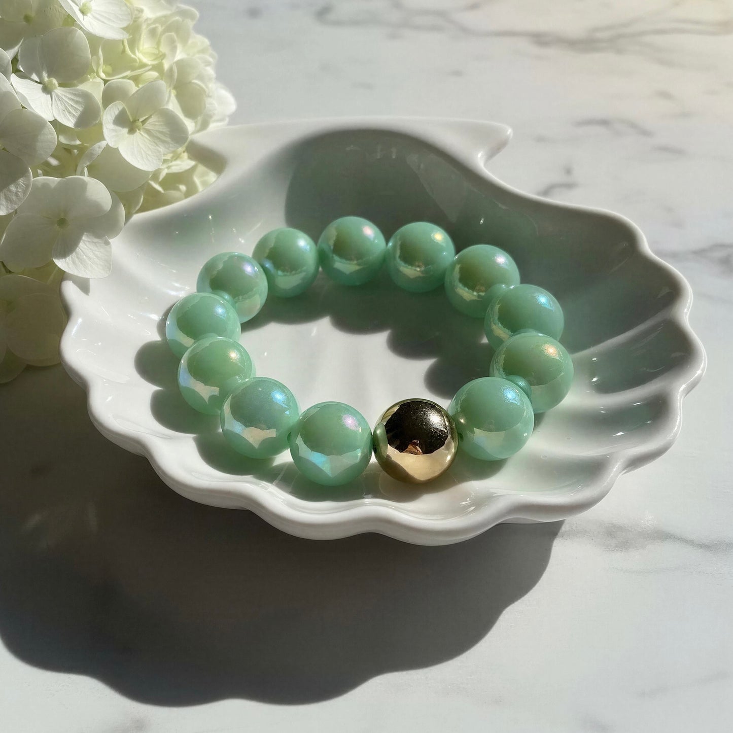 The Mint Glow Bracelet on a white dish, surrounded by white flowers on a marble surface.