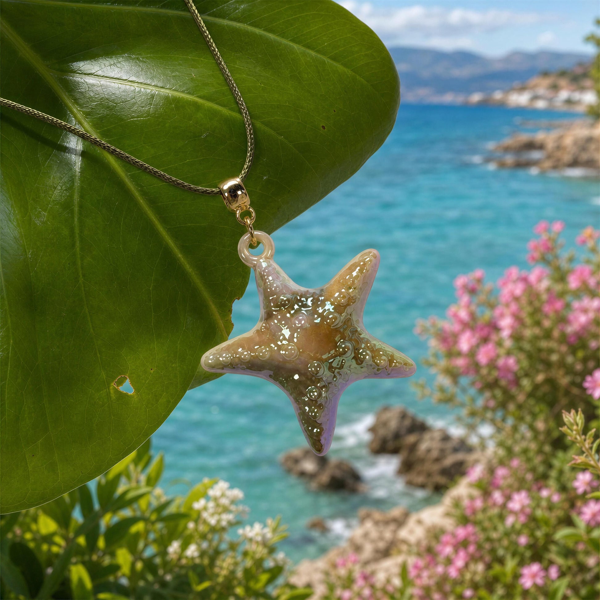 The Nerina Olive Necklace hanging from green leaf by Mediterranean coast.