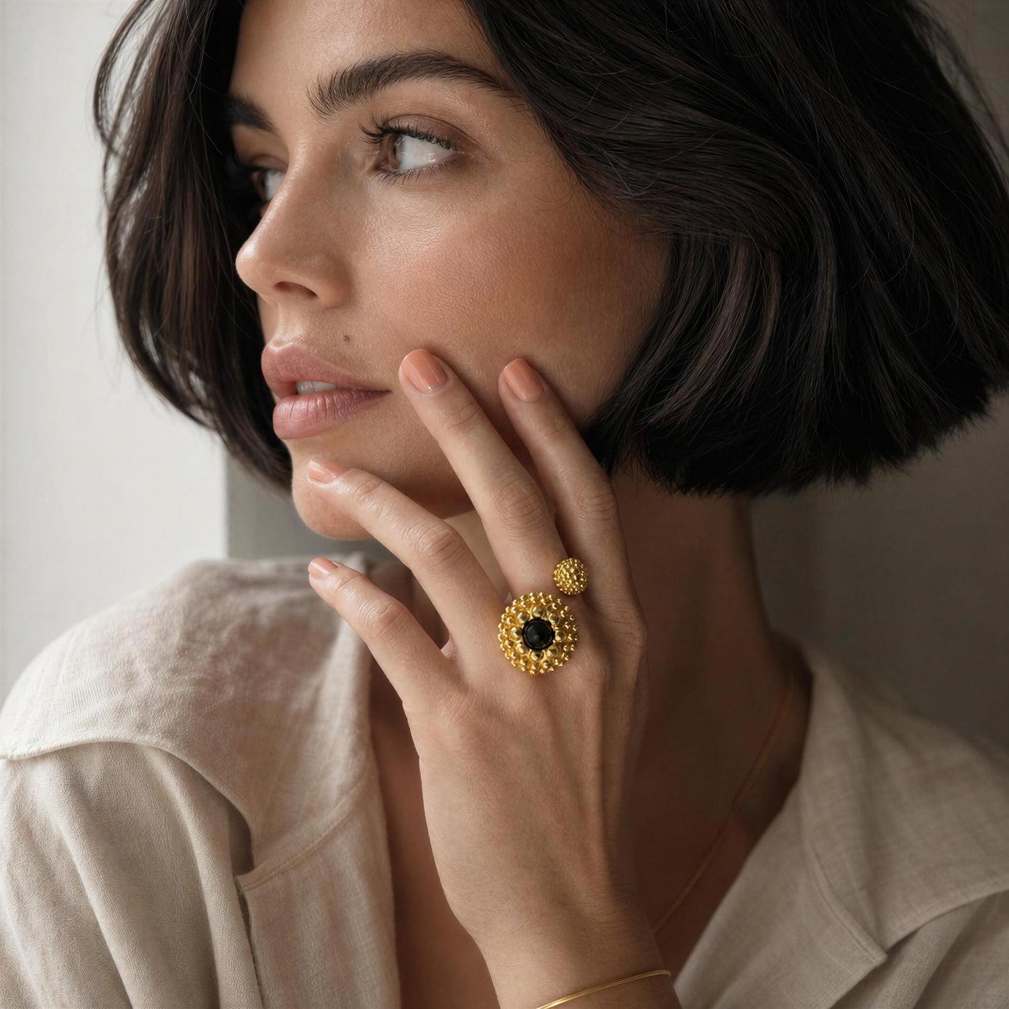 A close-up lifestyle shot of a woman with a short dark bob, wearing a beige linen shirt and the Nero Ring from Chica Chica Jewelry.