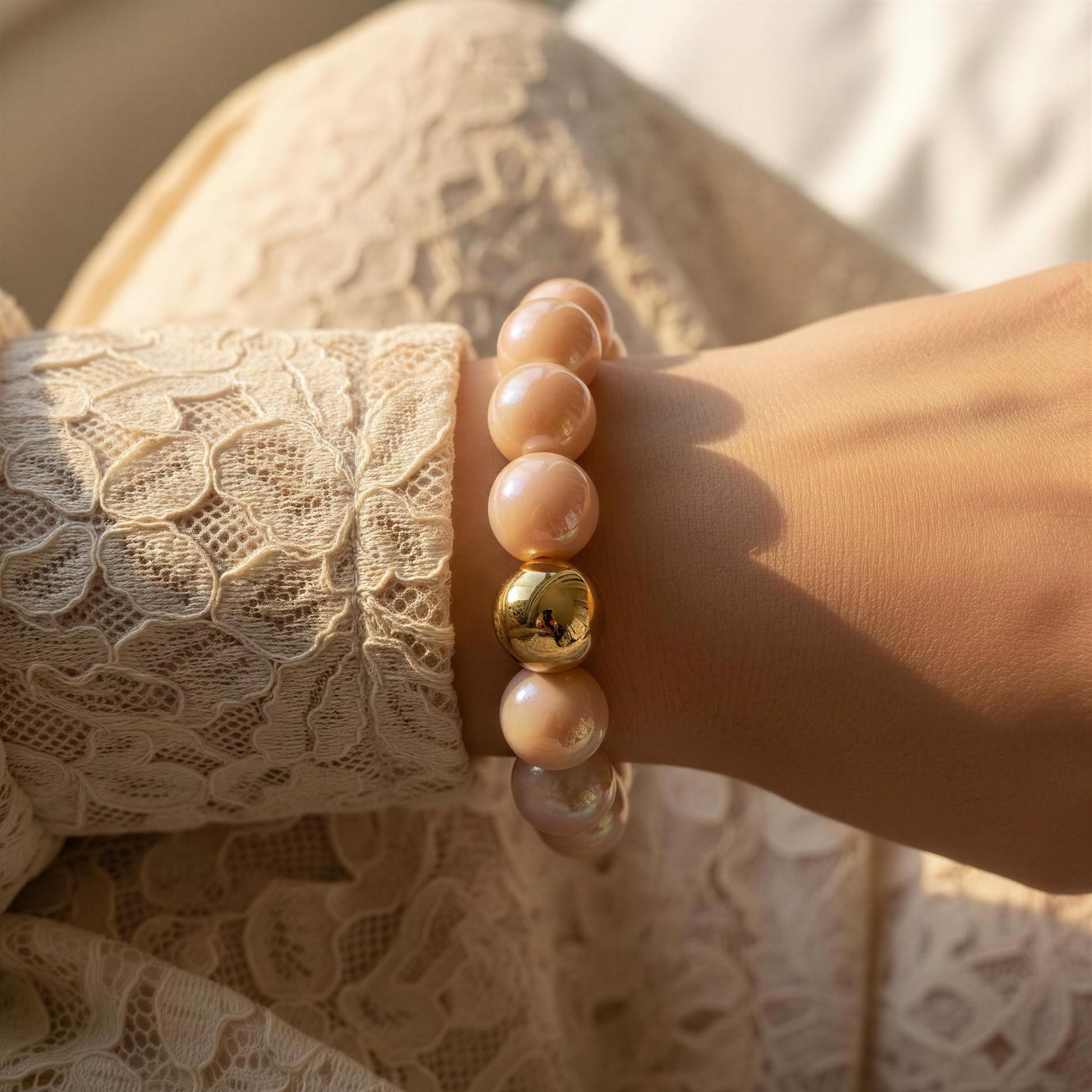 Close-up of a hand wearing the Peach Glow Bracelet with a blurred lace garment in the background.