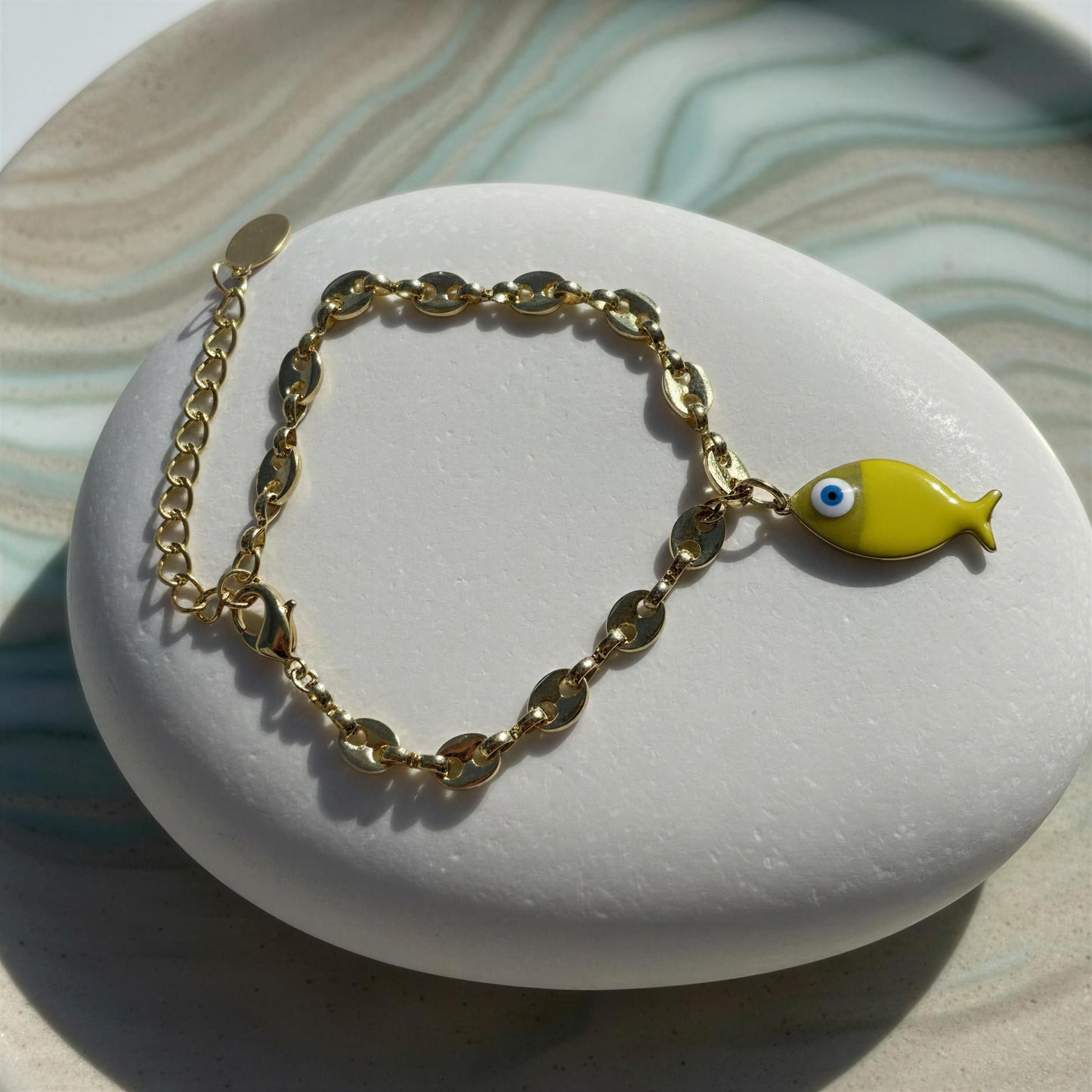 Gold chain bracelet with a yellow fish charm on a white stone