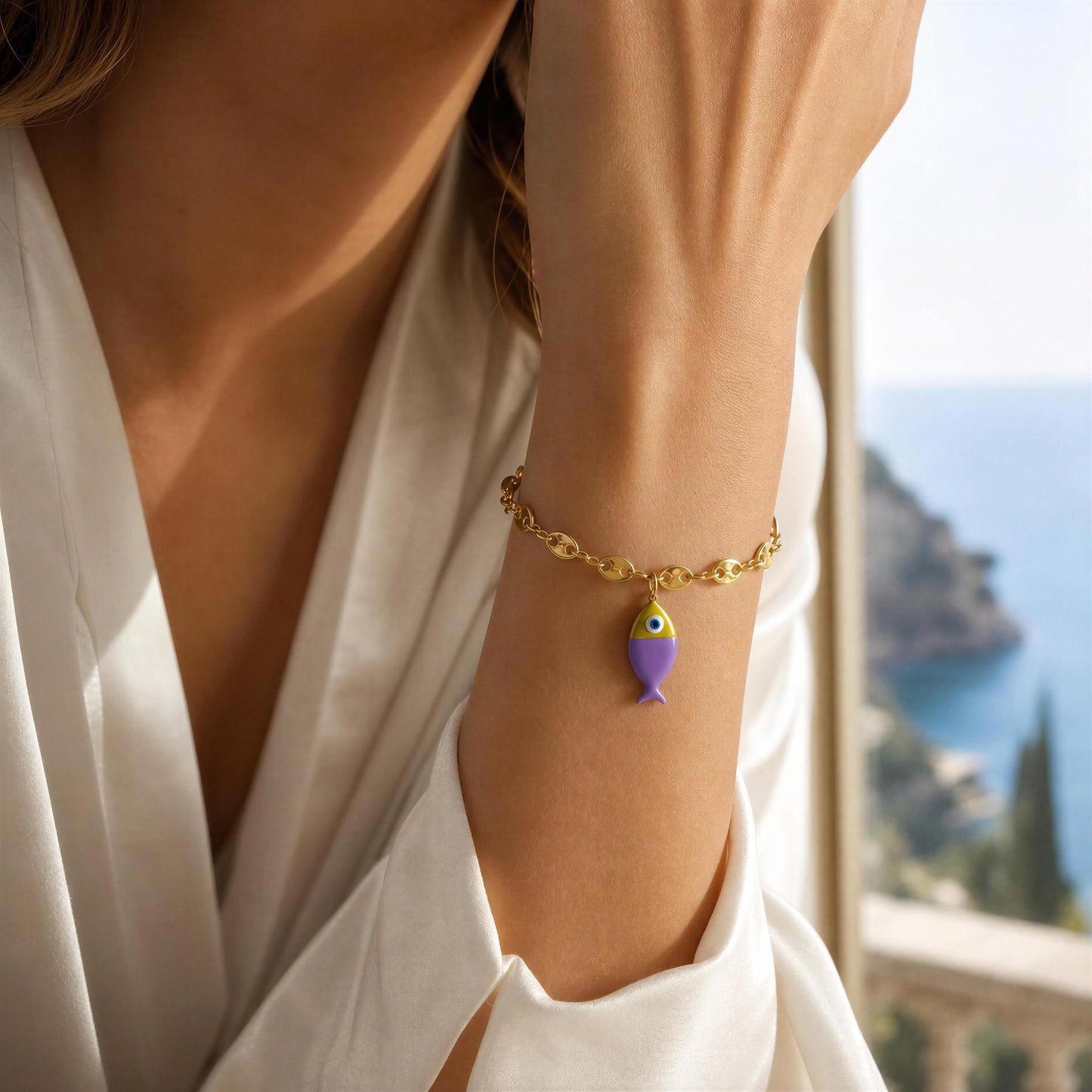 Gold bracelet with a purple fish charm on a person's wrist, with a scenic background.