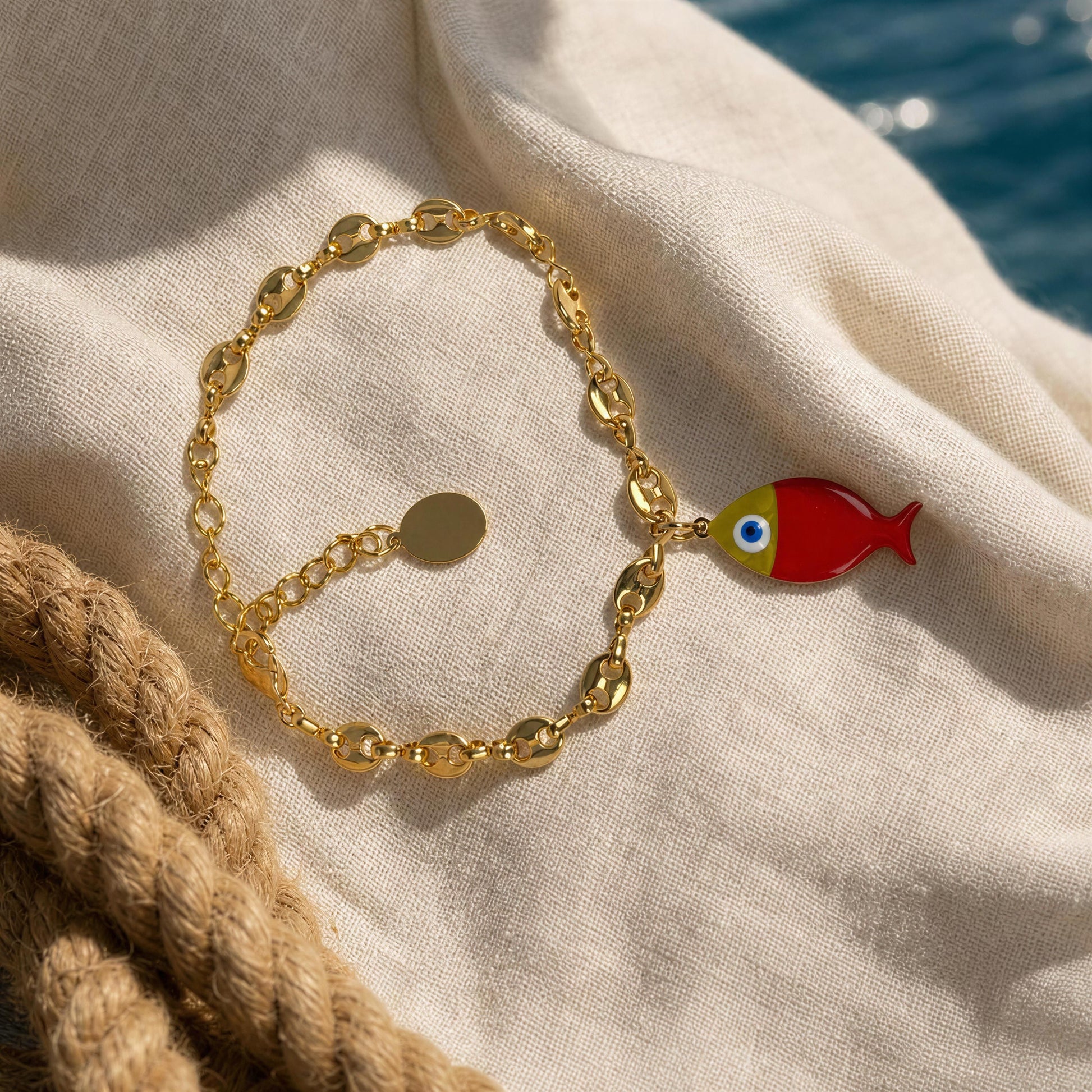 Gold bracelet with a red fish charm on a beige fabric background