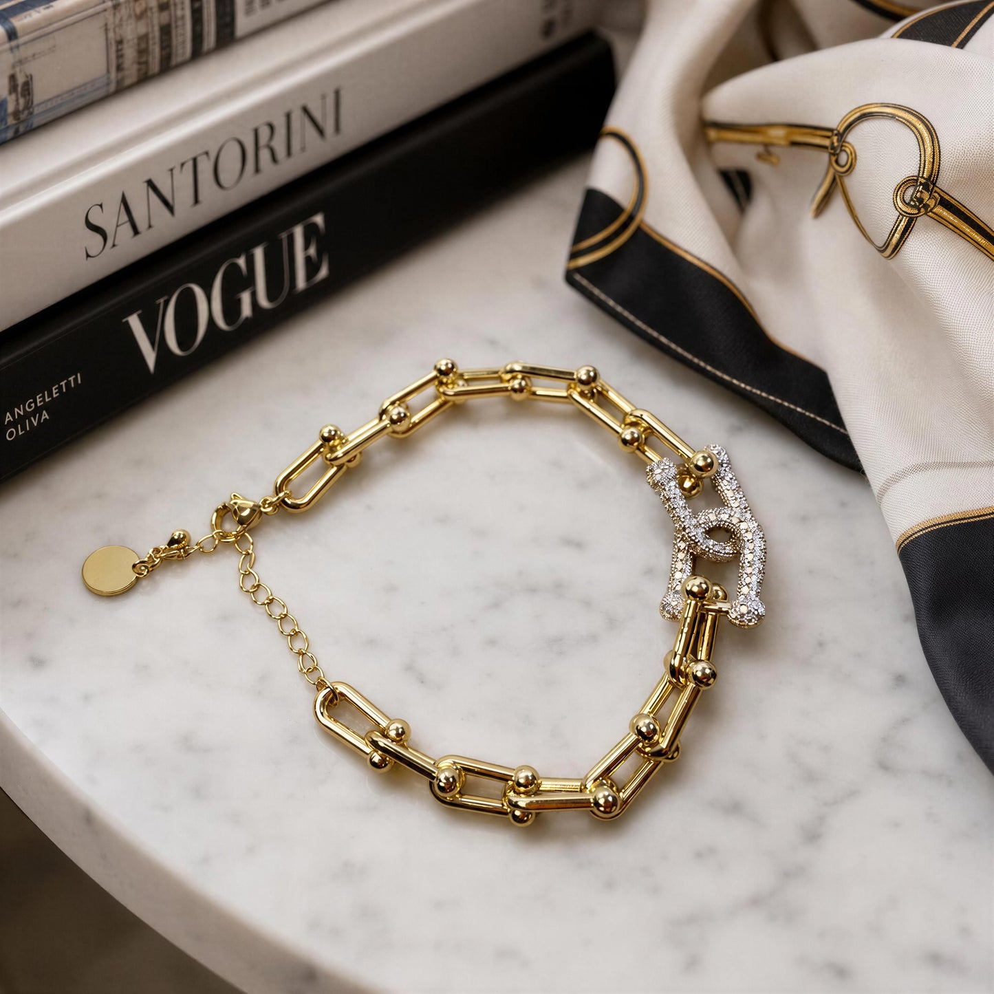 The Radiance Link Bracelet from Chica Chica Jewelry, styled on a white marble surface next to a black and white scarf and books.