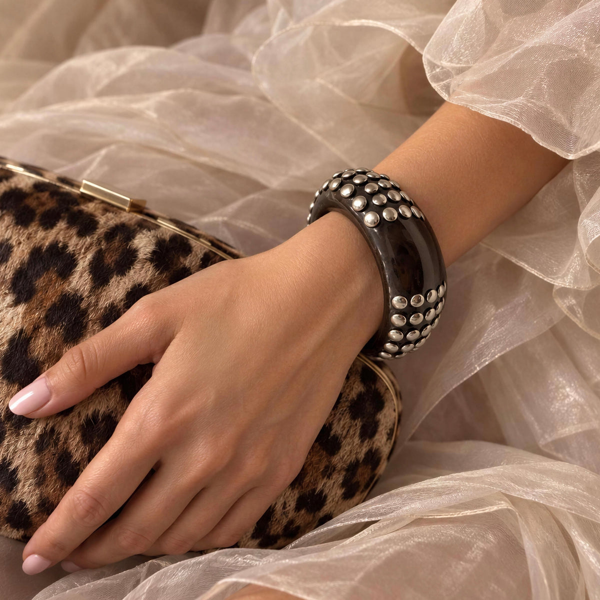 Model wearing the  Rivoli_Bangle from _Chica_Chica_Jewelry, a dark resin bangle with silver-tone stud detailing.