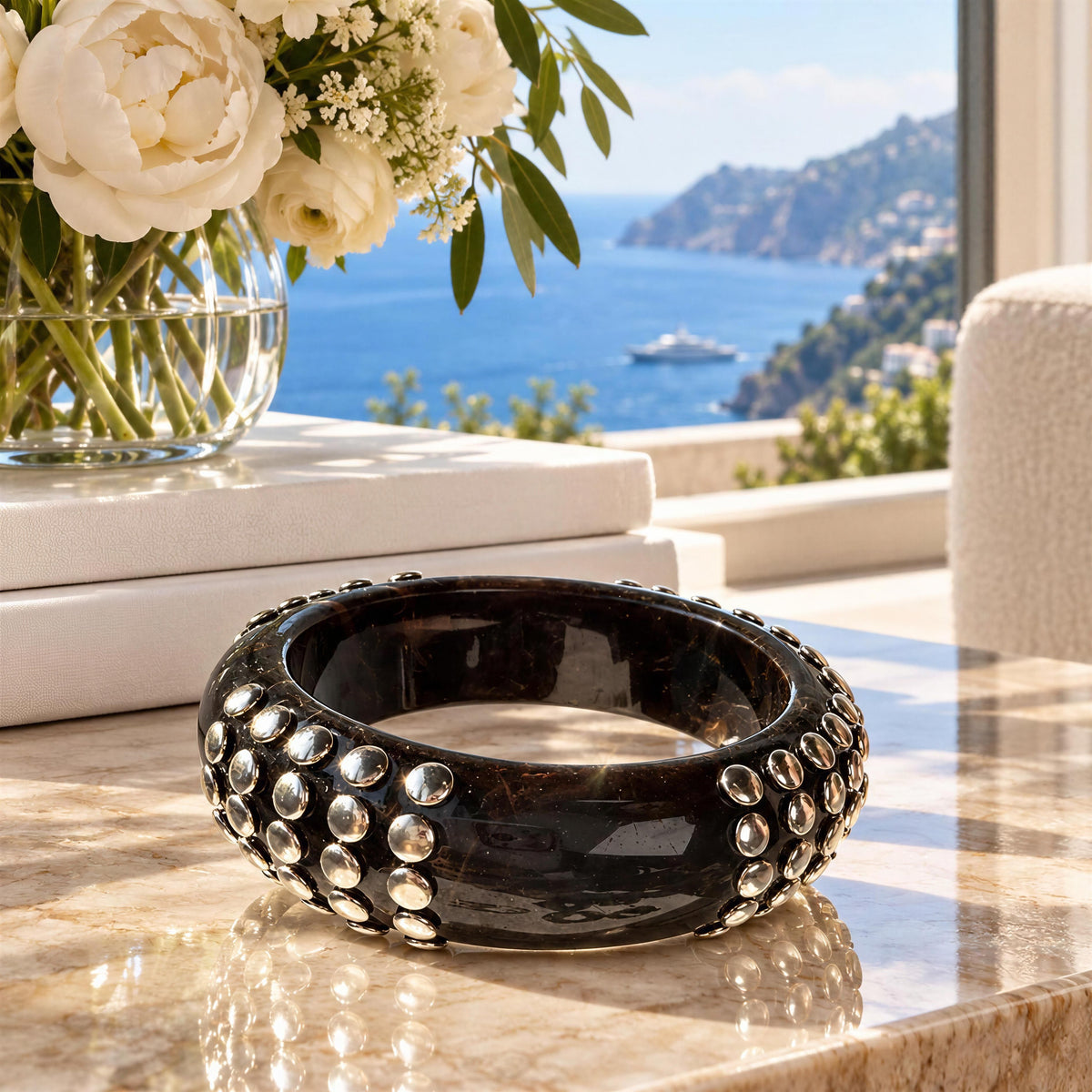 The Rivoli Bangle from Chica Chica Jewelry against a marble table with Mediterranean view.
