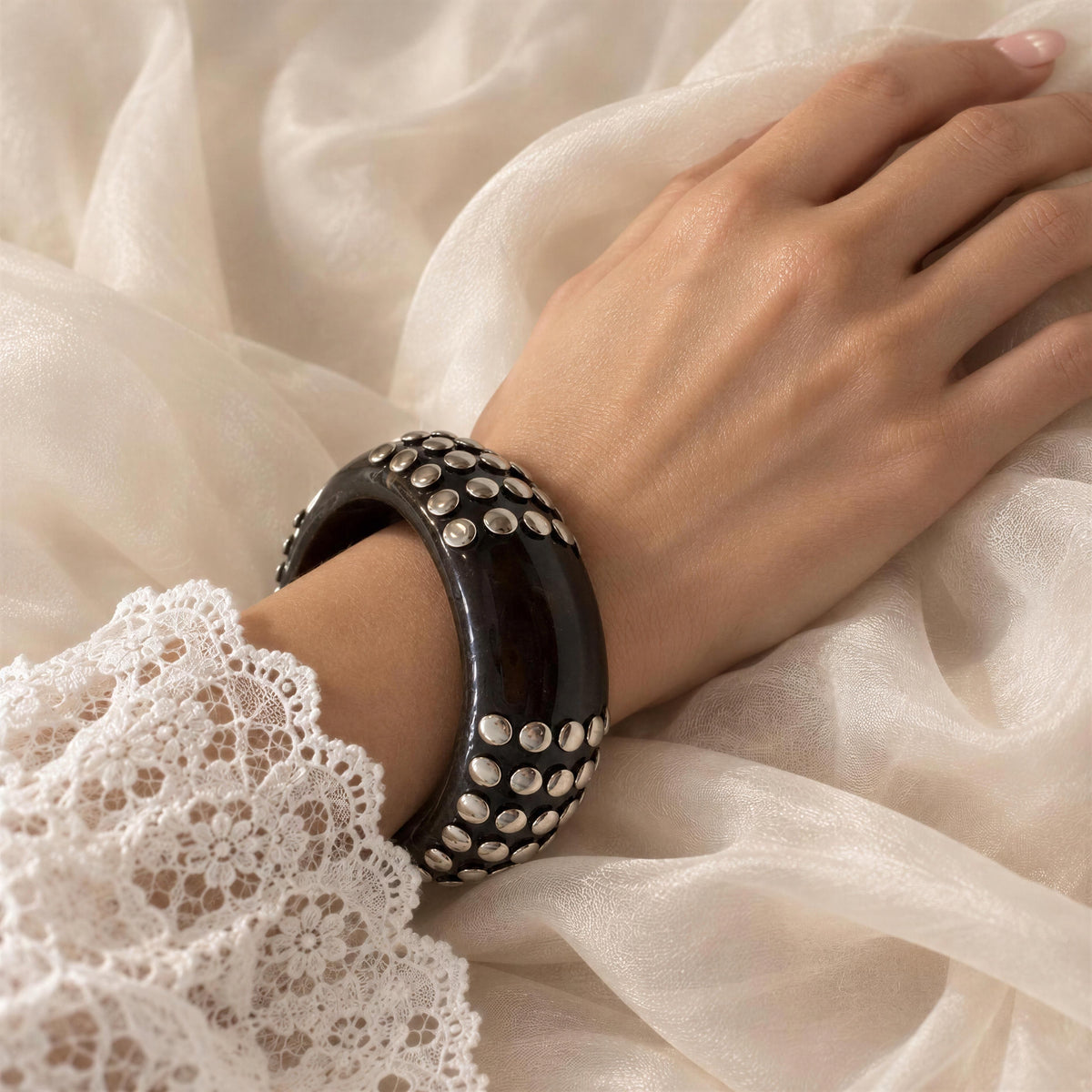 Model wearing the Rivoli Bangle from Chica Chica Jewelry, a dark resin bangle with silver-tone stud detailing.