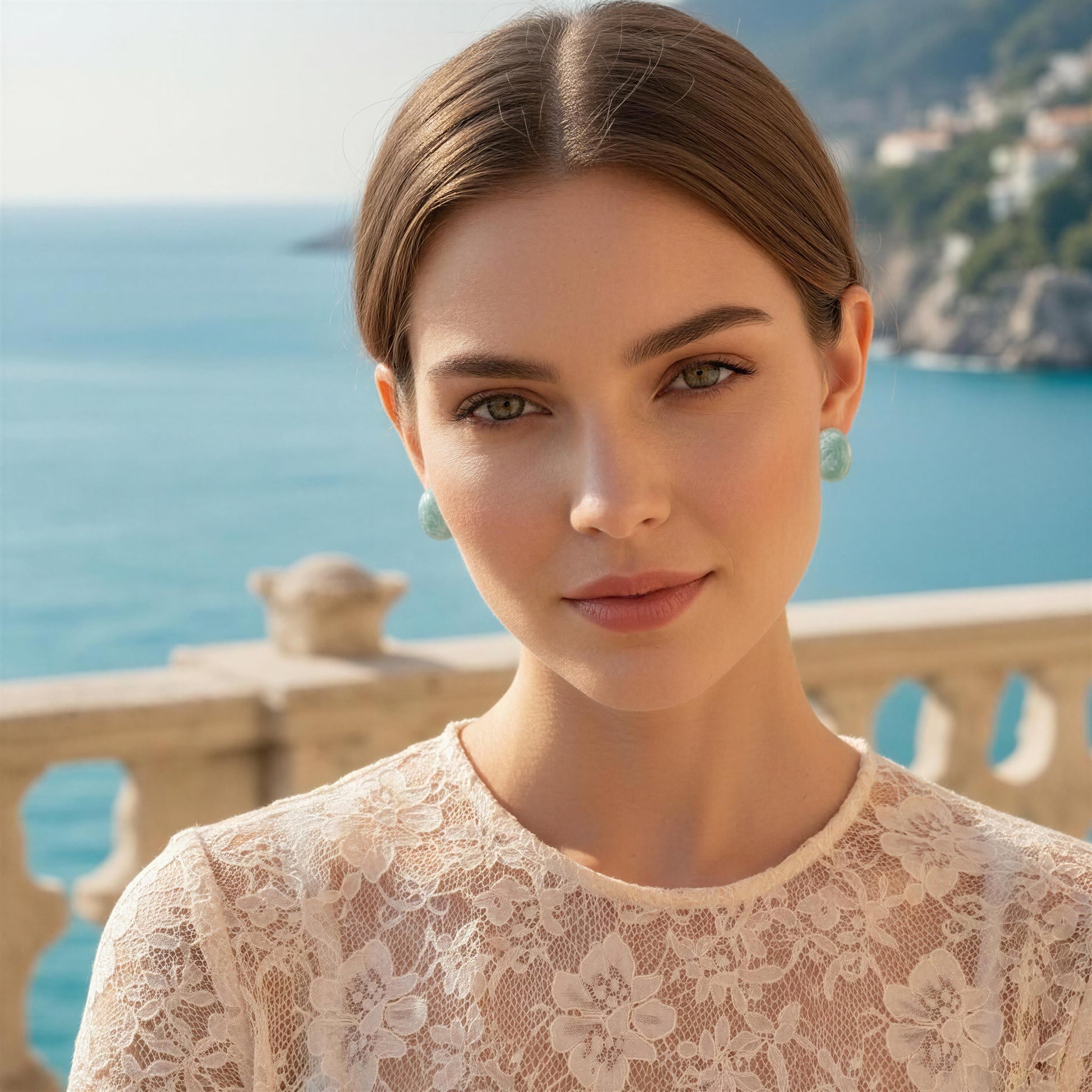 Woman in a lace dress wearing the Rosina Studs -Aqua Glow standing in front of a scenic ocean view.
